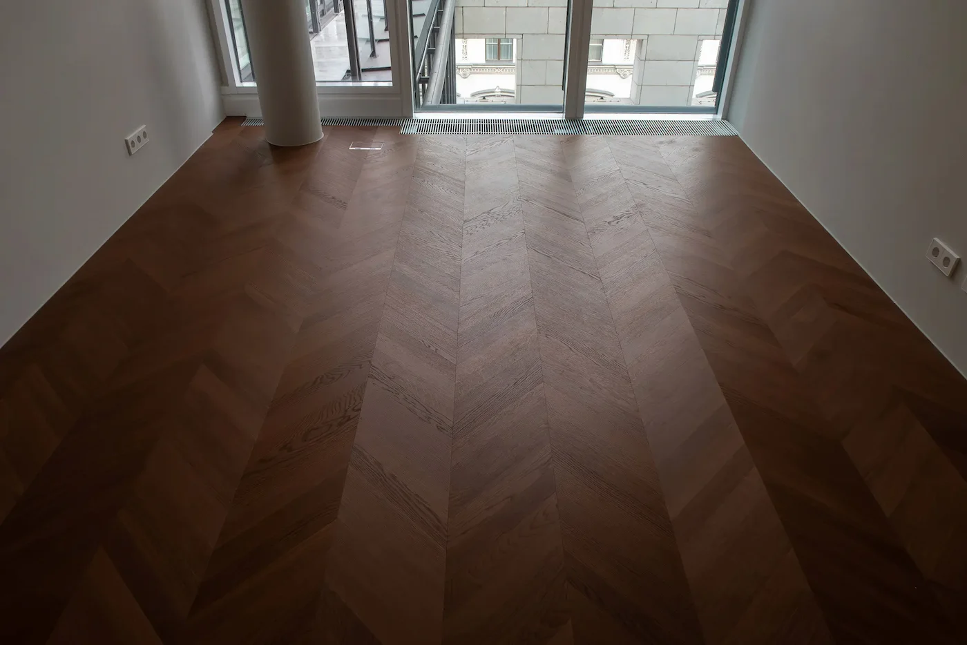 Großer Wohnraum mit gebogener Fensterfront und hochwertigem Chevron-Parkettboden.