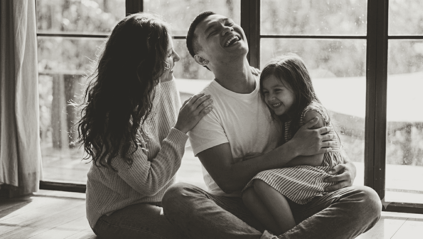 A dad holds his daughter, mum sits nearby - all laughing