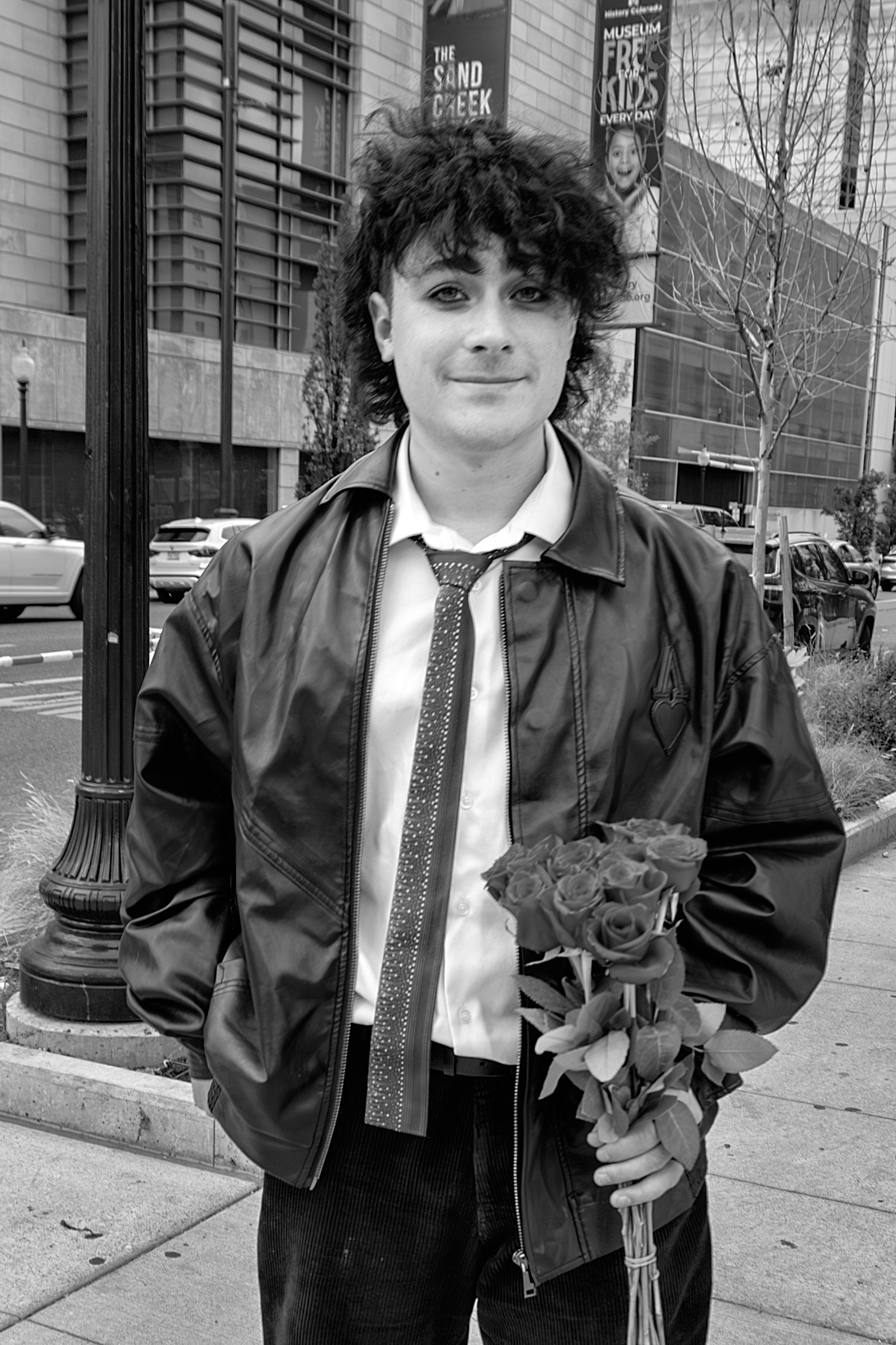 Young man holding a bouquet of roses, dressed in a loose tie and jacket, standing on a city street