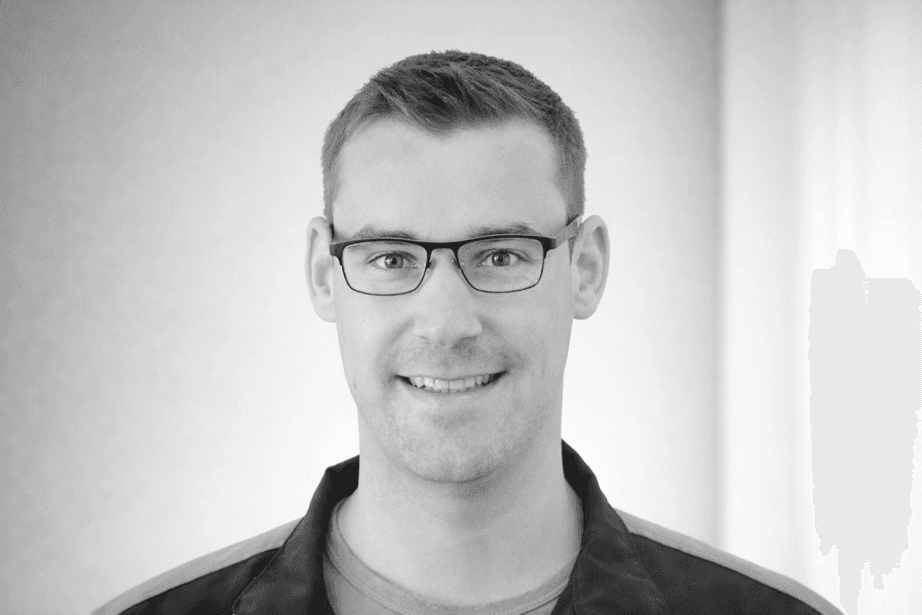 Portrait of a smiling man wearing glasses in black and white. He is looking at the camera.