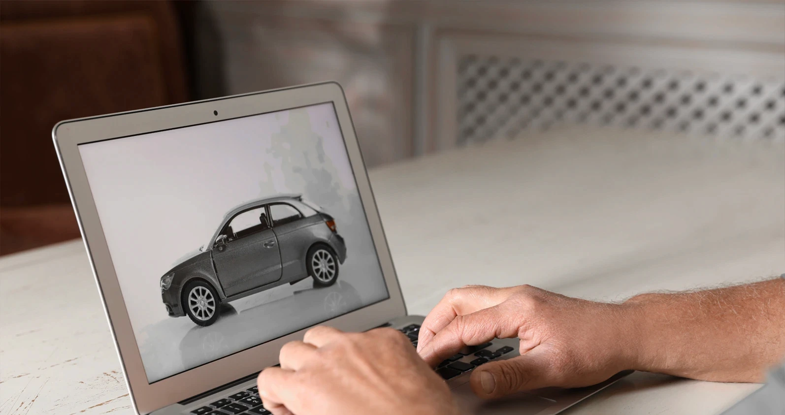 Man using laptop to buy car at wooden table indoors, closeup