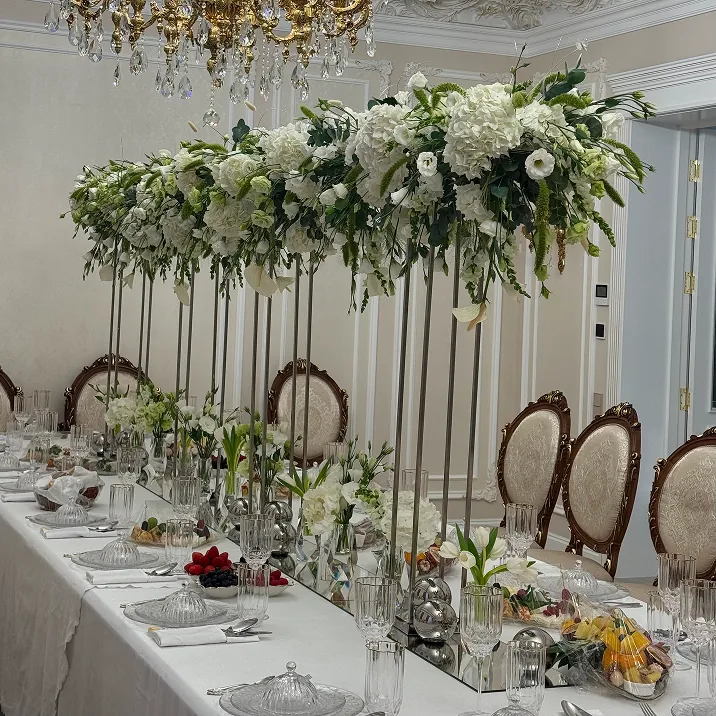 Formal dining table with tall white floral centerpieces, crystal glassware, fruits, and appetizers, surrounded by ornate chairs in a classic, luxurious room.