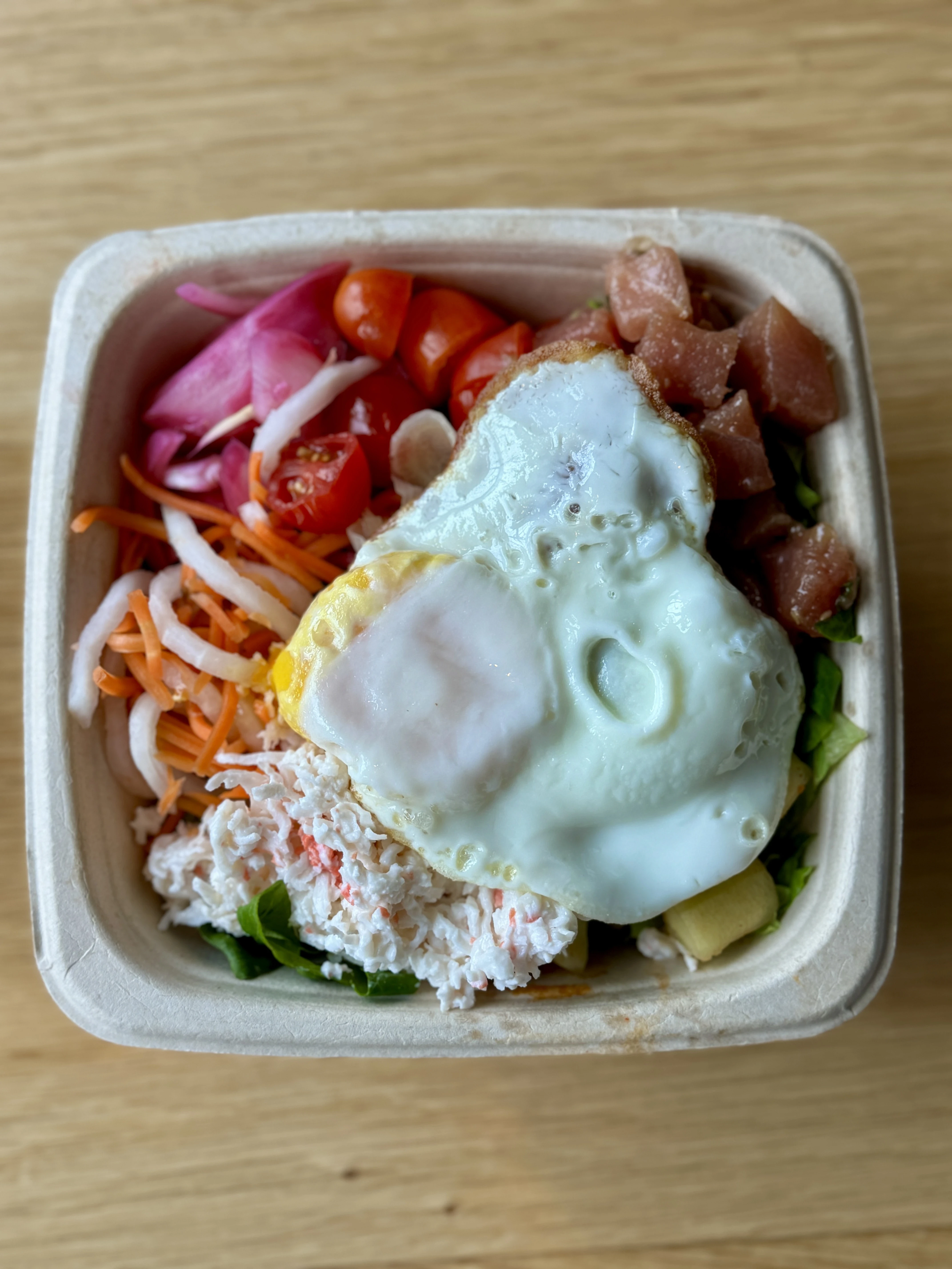 Bul Box asian fusion poke bowl with egg, tuna poke, pickled onions, crab salad, tomatoes, lettuce, and rice