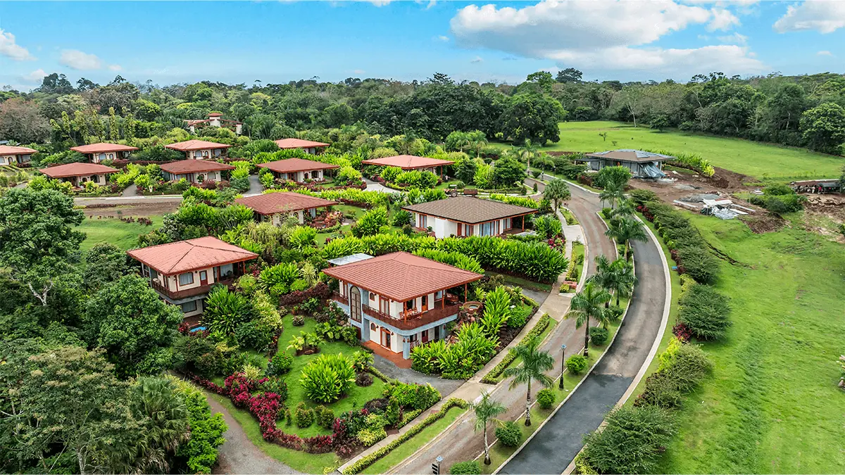hills-costa-rica.webp Aerial view of the Arenal Hills community, showing luxury villas with red-tile roofs, tropical landscaping, and a curving access road.