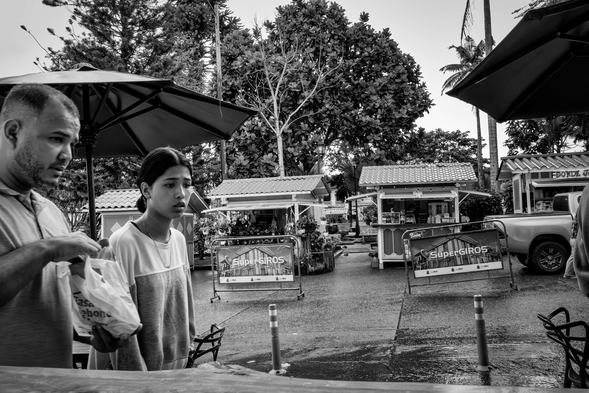 Rainy street scene with people passing by a bar window.