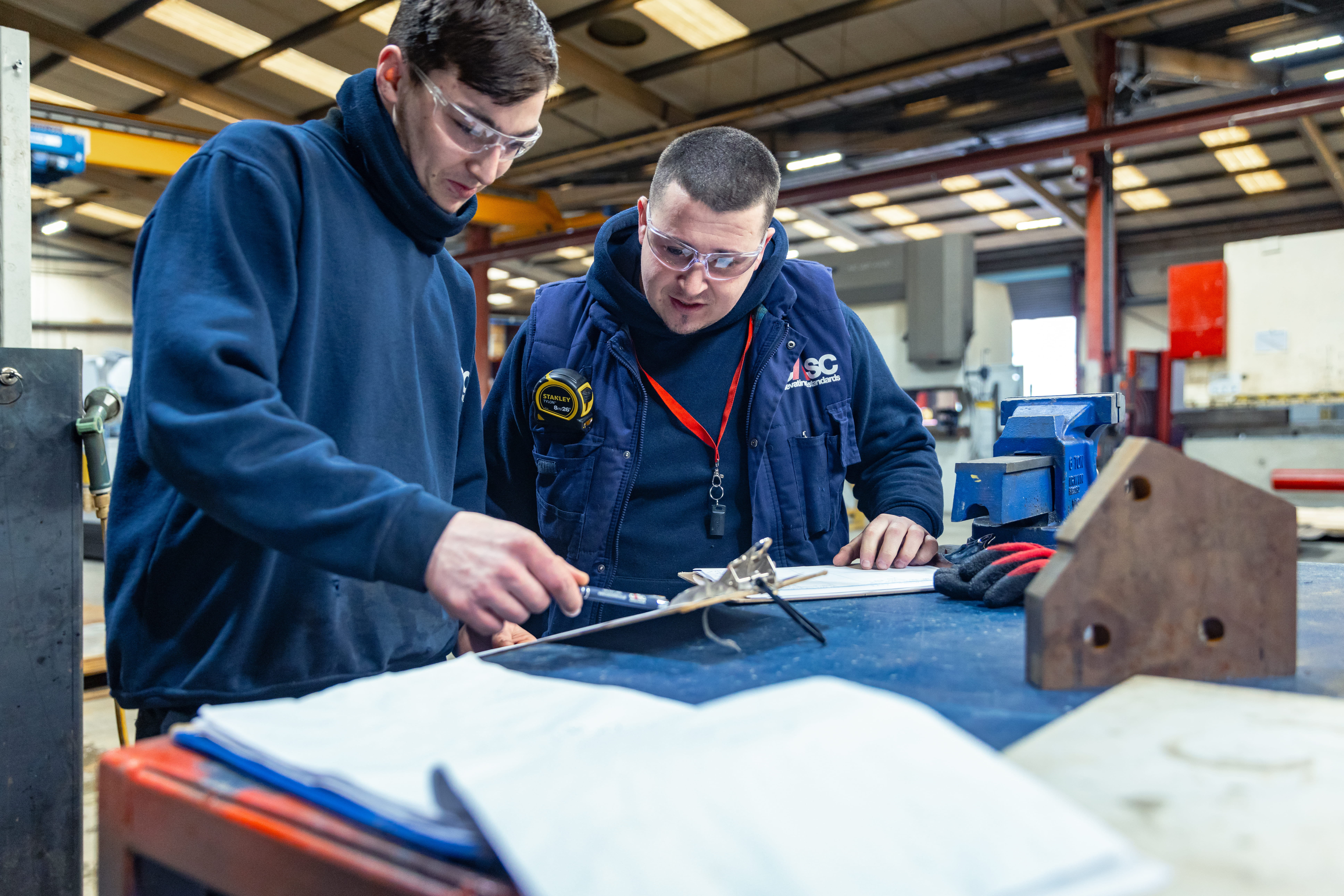 Two CASC workshop technicians reviewing technical drawings together at a workbench.