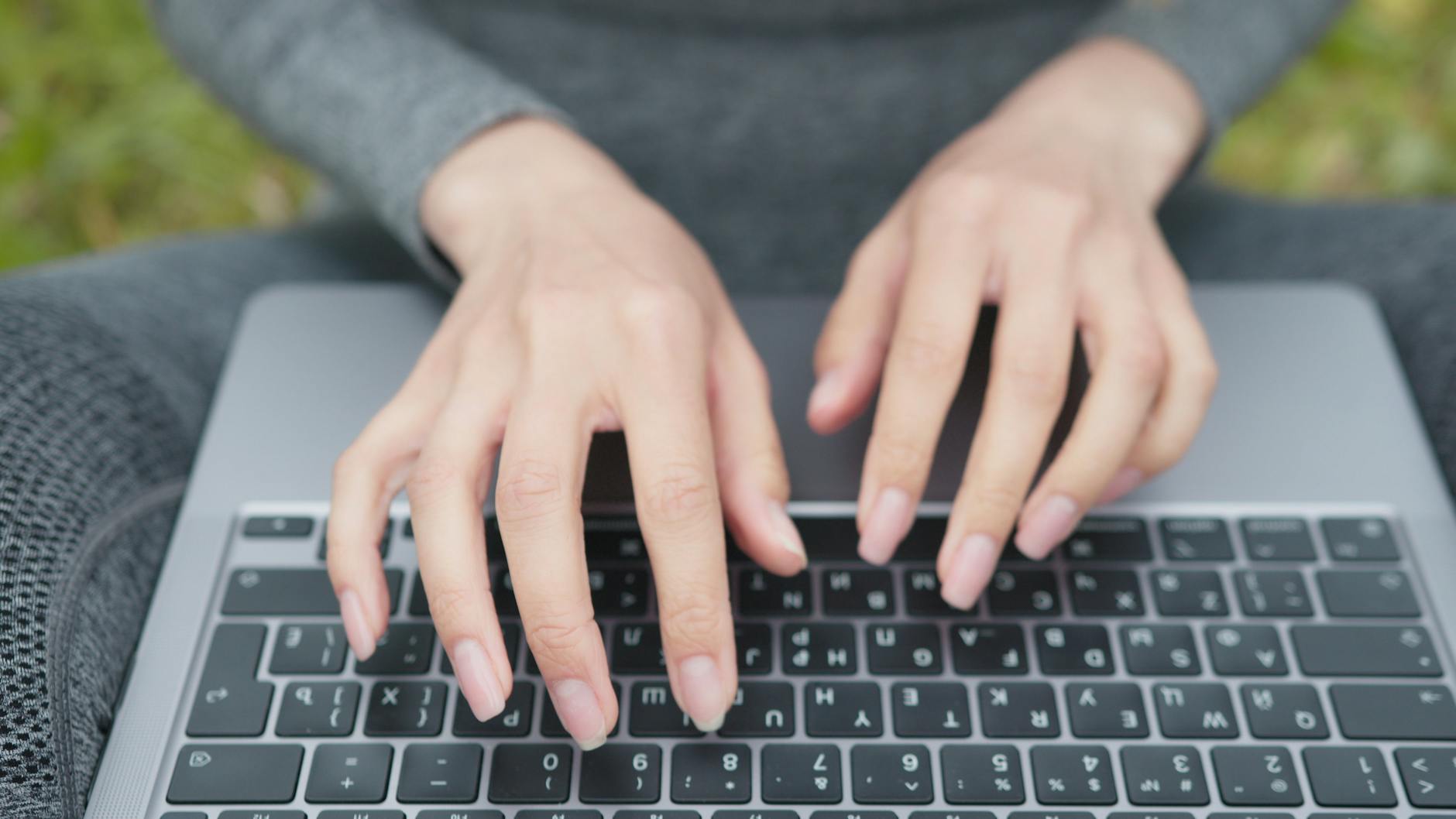 A person's hands typing on a laptop next to a cup of coffee and a printed instructional manual.