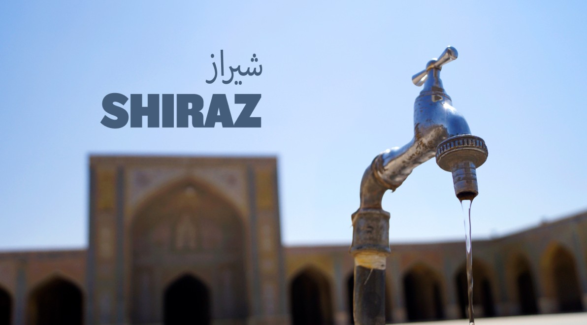 Water dripping from a vintage chrome tap in Shiraz, with a courtyard mosque iwan softly blurred in the background.