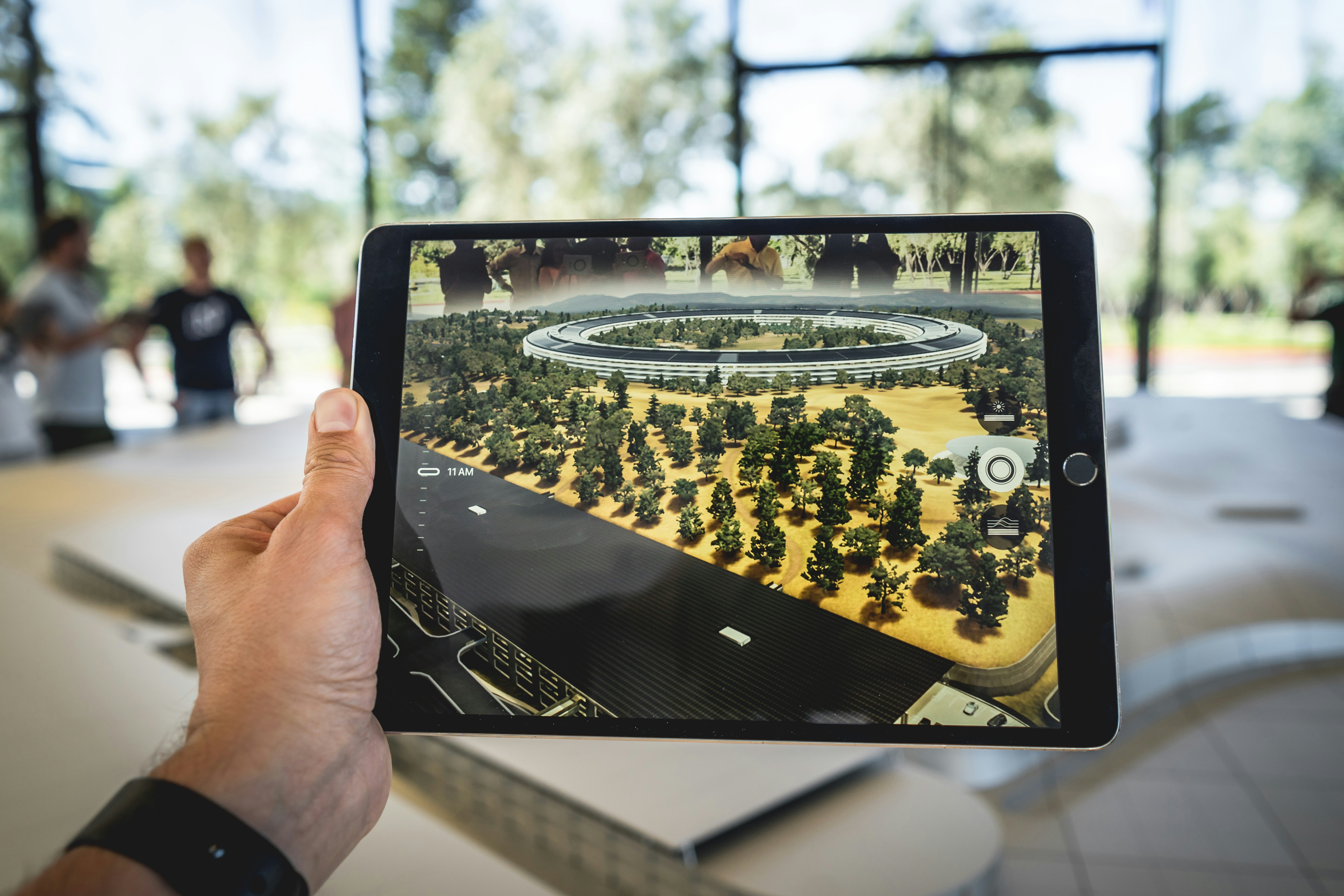 This image features a hand holding a tablet displaying a detailed augmented reality model of a large building complex, exemplifying the powerful applications of AR marketing. The digital model seamlessly integrates with the real-world environment, illustrating how Augmented Reality marketing can transform traditional advertising and presentations into engaging, interactive experiences. The realistic 3D rendering of the building complex highlights the potential of AR marketing apps, where users can explore virtual content layered onto physical spaces. This setup emphasizes the role of AR marketing developers in creating interactive visualizations that captivate audiences and provide businesses with innovative ways to showcase products and services. The use of augmented reality in this image showcases how brands can use AR technology to create immersive marketing campaigns, revolutionizing customer engagement by allowing users to interact with virtual models in real time.