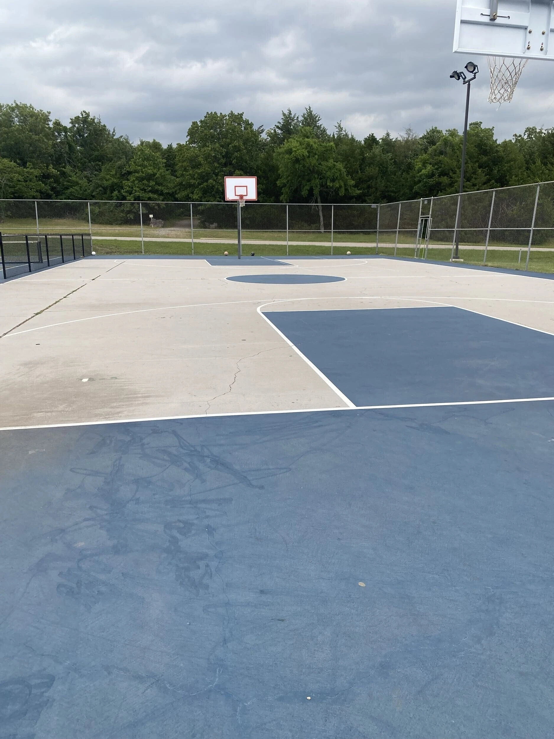 Worn basketball court with faded paint and surface cracking before resurfacing at Bell Park in Greenwood, AR