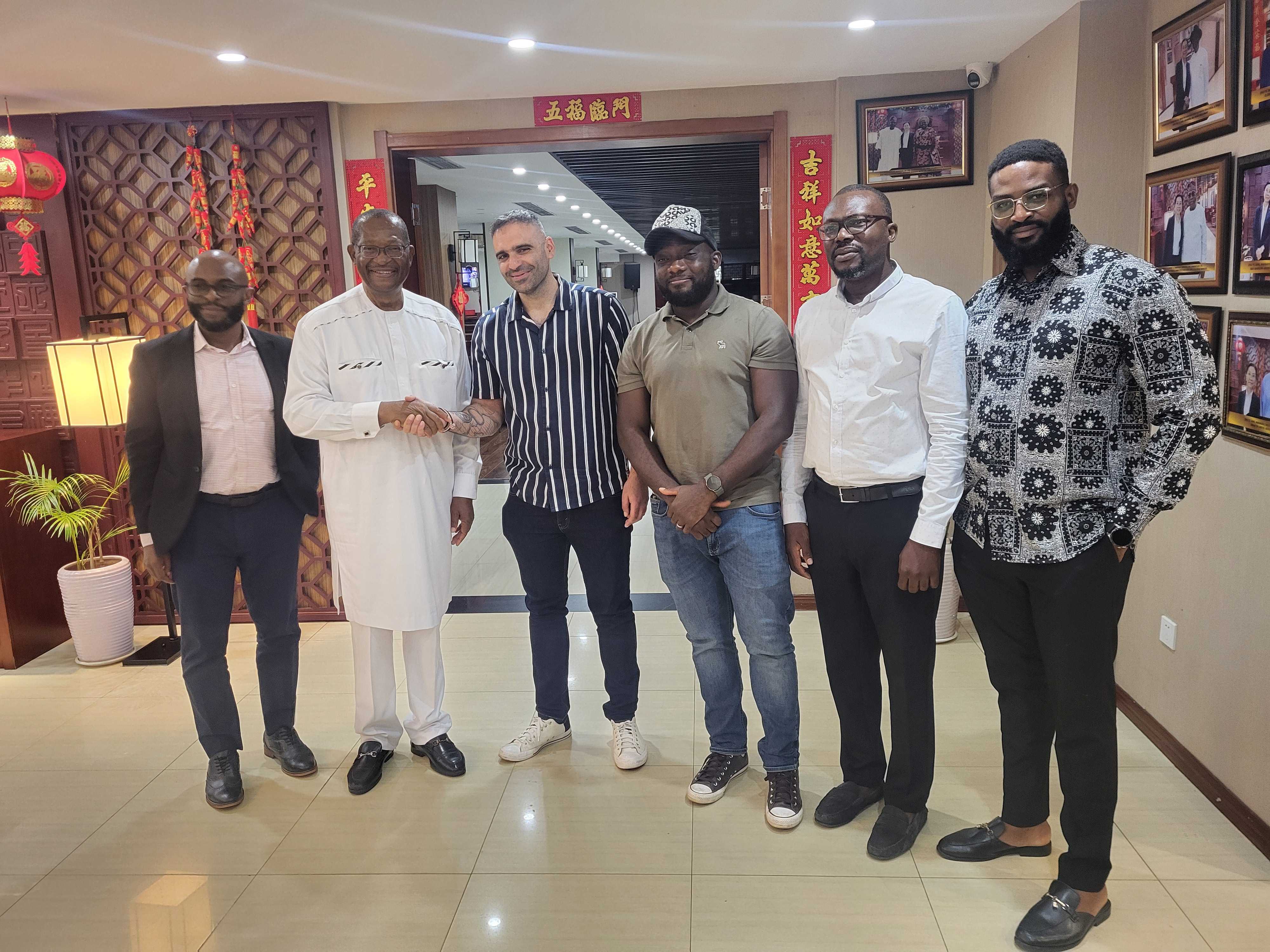 A man and woman sit on beige chairs in a modern room with a red paneled wall. A red pendant light hangs above a wooden coffee table between them.