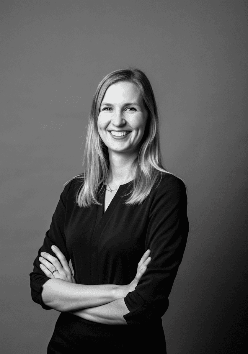 Black and white portrait of a smiling woman with blonde hair and crossed arms, exuding confidence and warmth.
