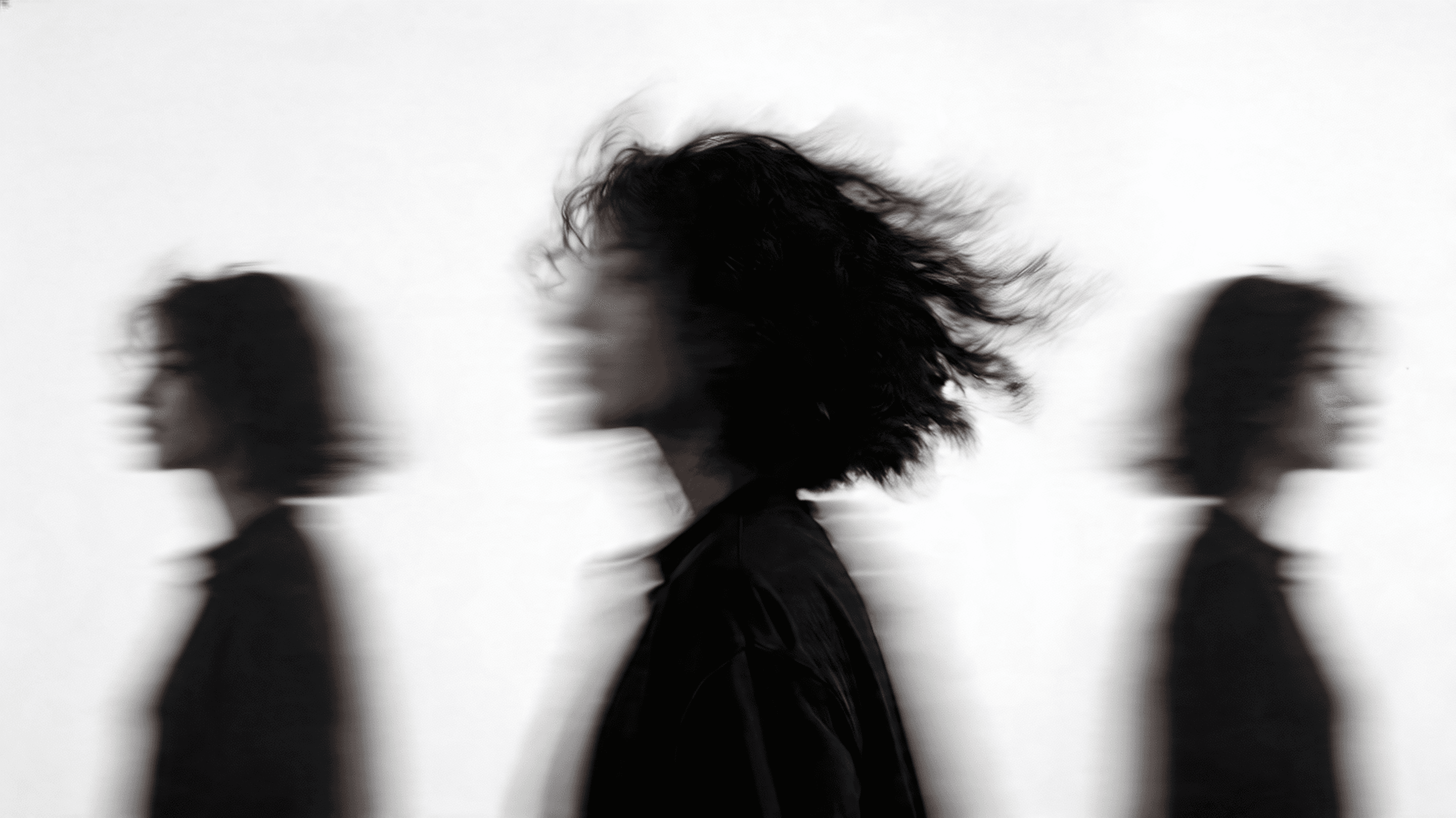 A black-and-white profile silhouette of a person with wind-blown hair, captured with a soft motion blur effect against a stark white background.