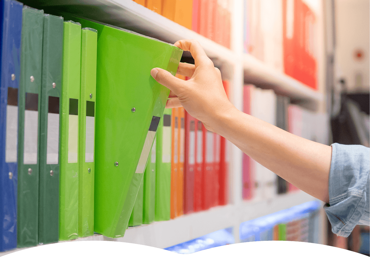 A person selects a vibrant green binder from a neatly arranged shelf of colorful office supplies, highlighting organization and choice in stationery.