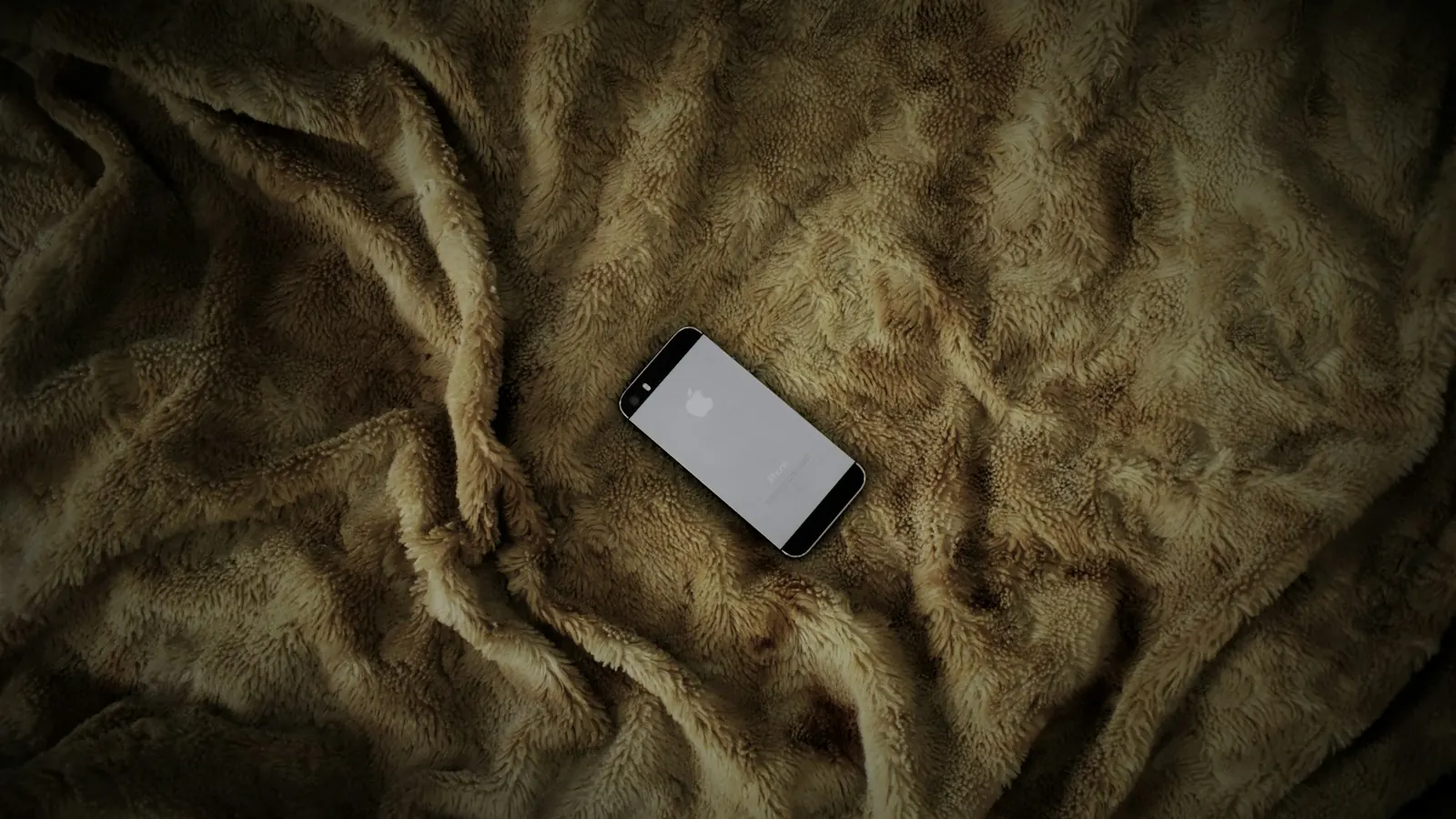 Ein Smartphone liegt mit dem Bildschirm nach unten auf einer zerknitterten braunen Plüschdecke