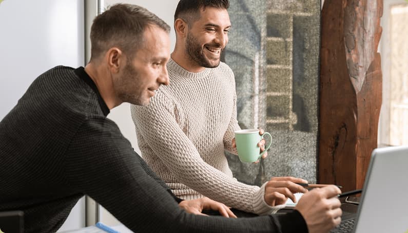 Twee mannen werkend aan een laptop in een moderne kantooromgeving, lachend en in gesprek.