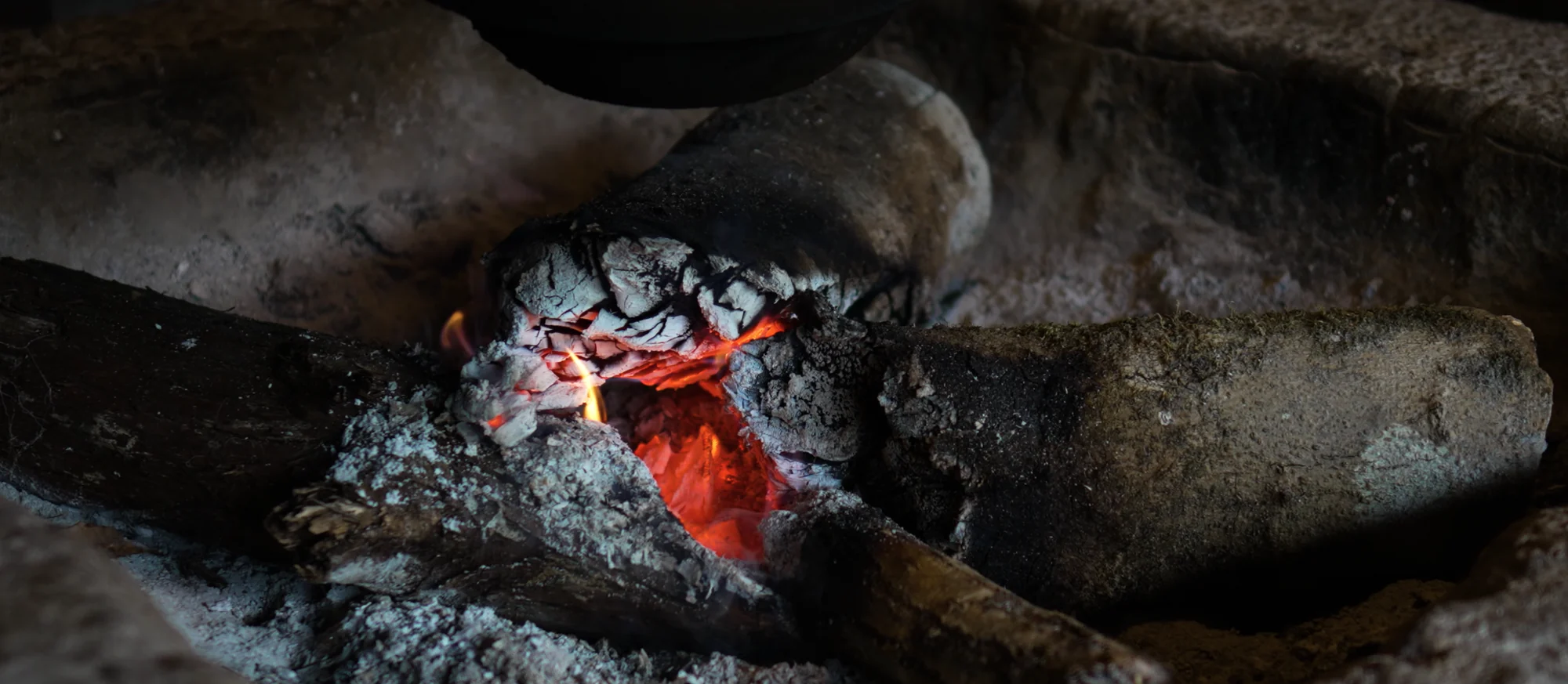 Close detail of glowing charcoal embers banked in ash in an irori hearth