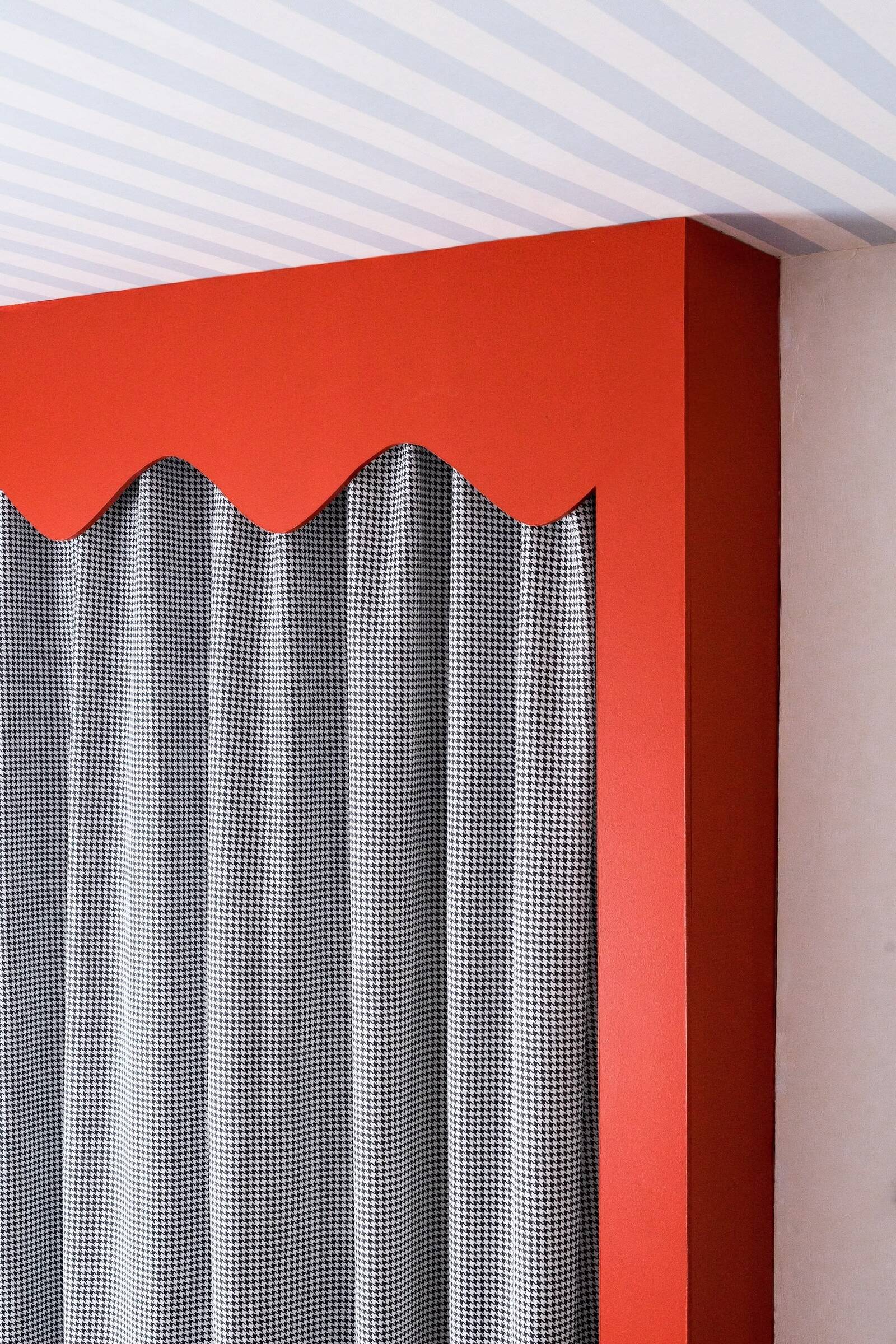 Teen bedroom with red scalloped custom joinery wardrobe, dogtooth print curtains, blue and white striped ceiling wallpaper, vibrant playful colour palette