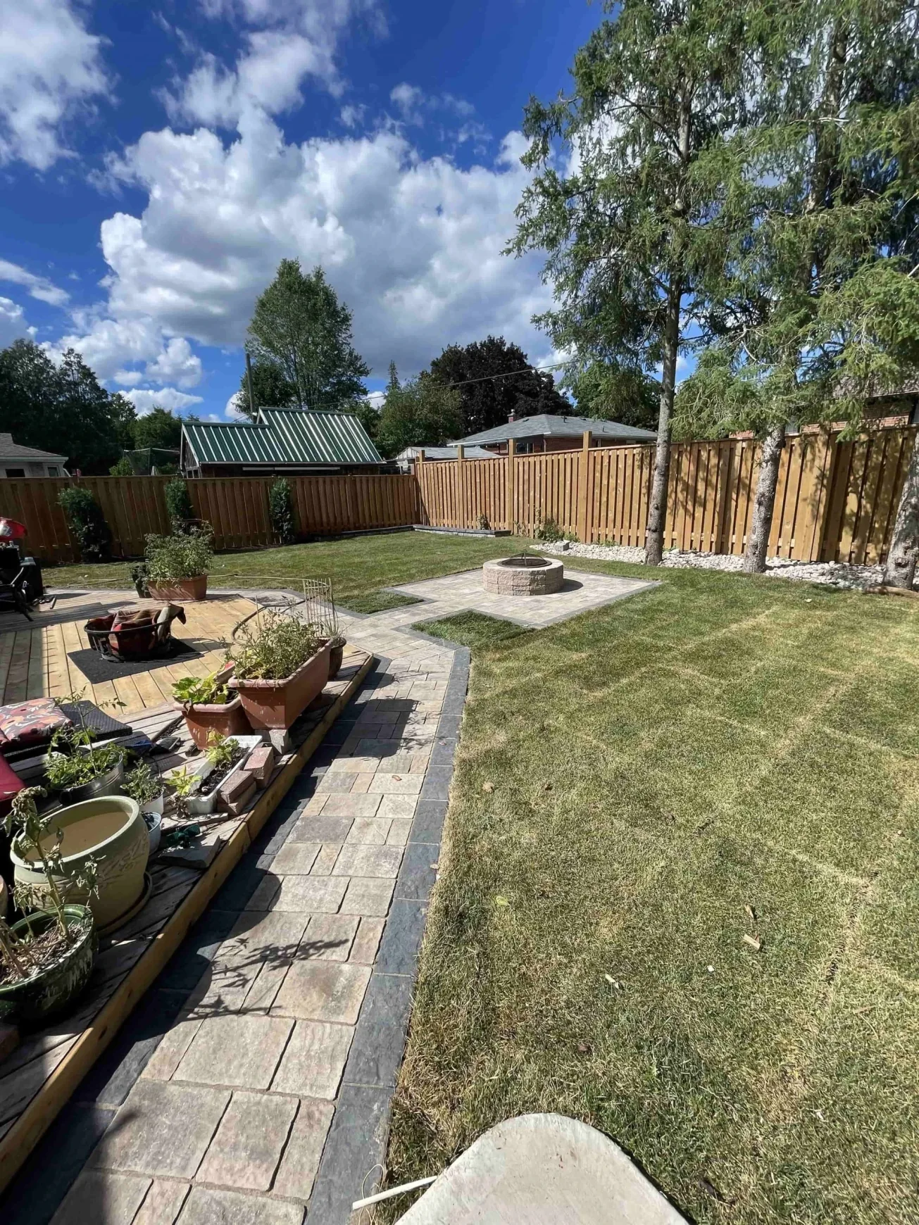 Backyard with interlocking pathway leading to a central fire pit surrounded by freshly laid sod.