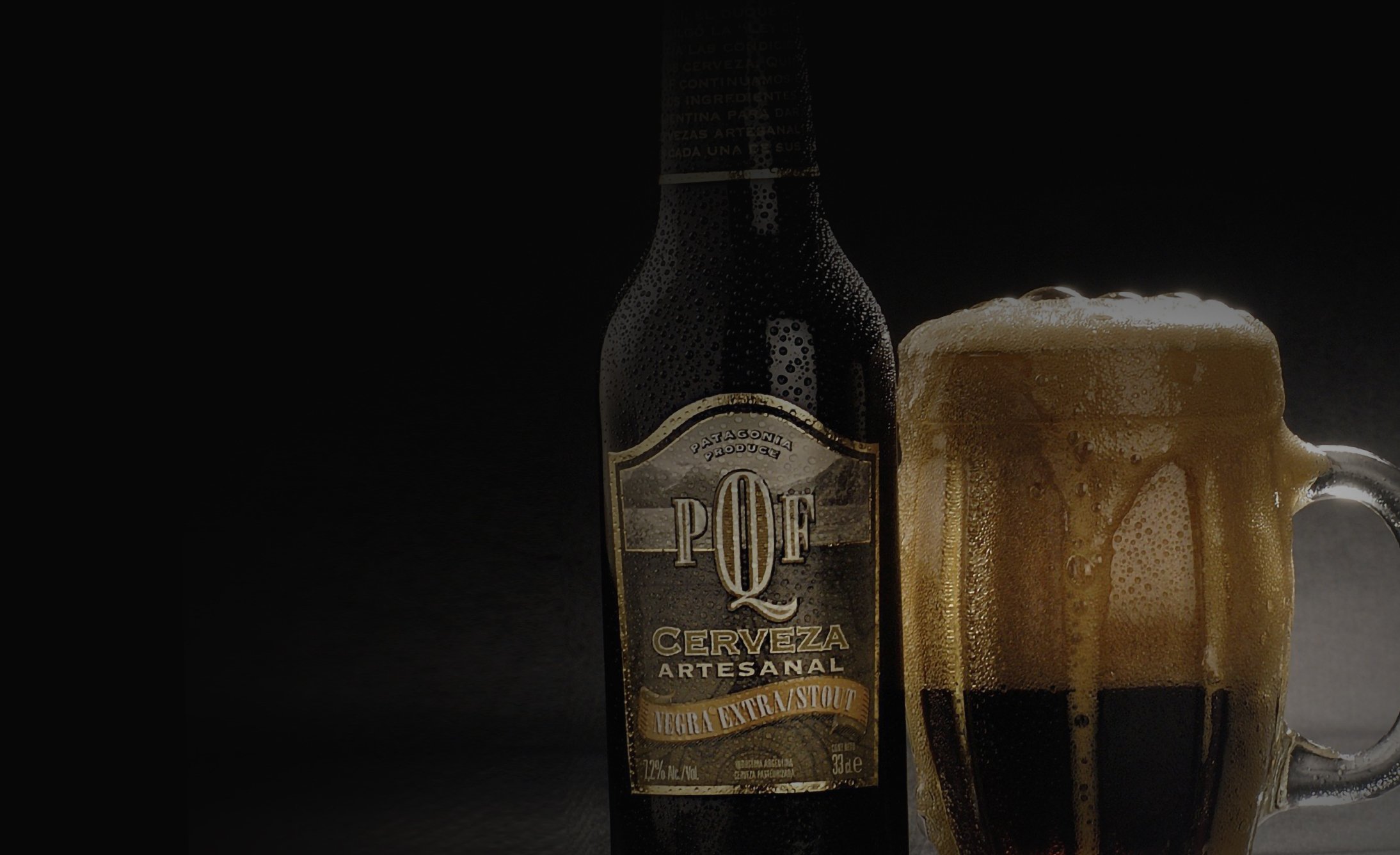 A dark beer bottle labeled "PQF Cerveza Artesanal" sits beside a frothy, full mug of beer on a black background, conveying a sense of richness.