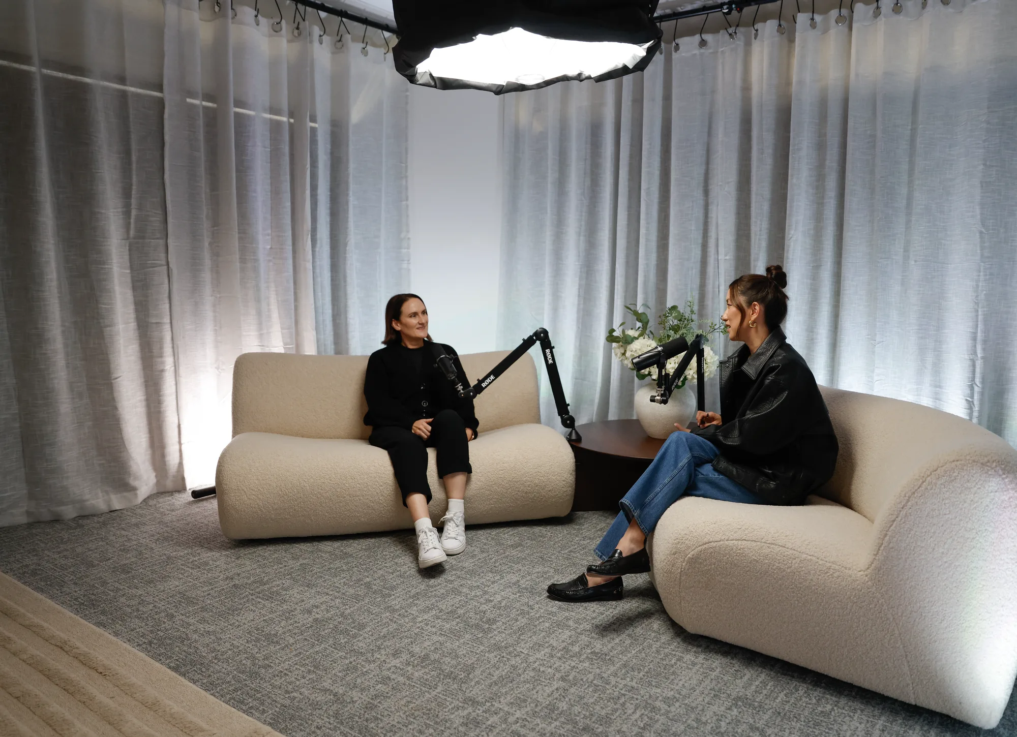 Two guests recording on cream sofas, seen from across the studio