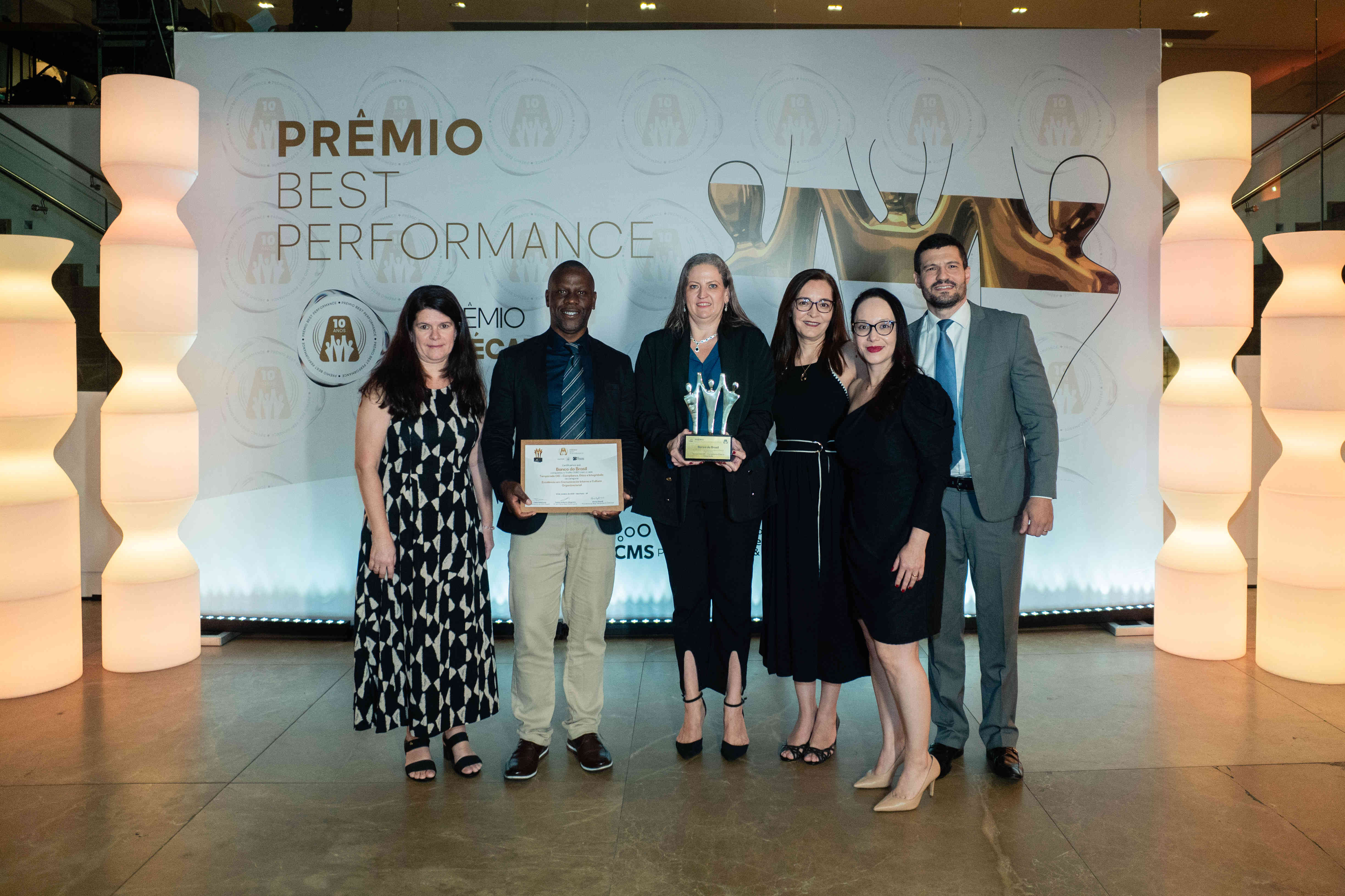 Executivos do Banco do Brasil posando com troféu ouro e certificado no palco do Prêmio Best Performance 2025