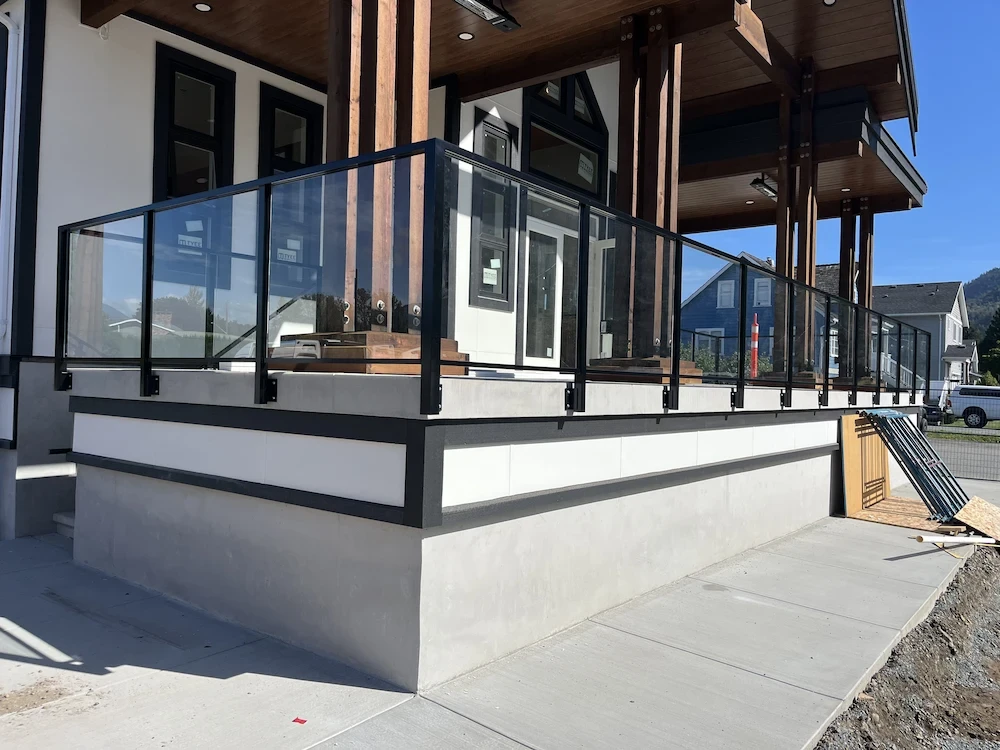 Modern front porch with black-frame glass railing and wood columns, combining clean lines with durable design for a residential entrance.