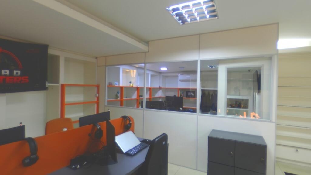 Espaço de trabalho da equipe UNEED, com estações laranja e divisórias de vidro