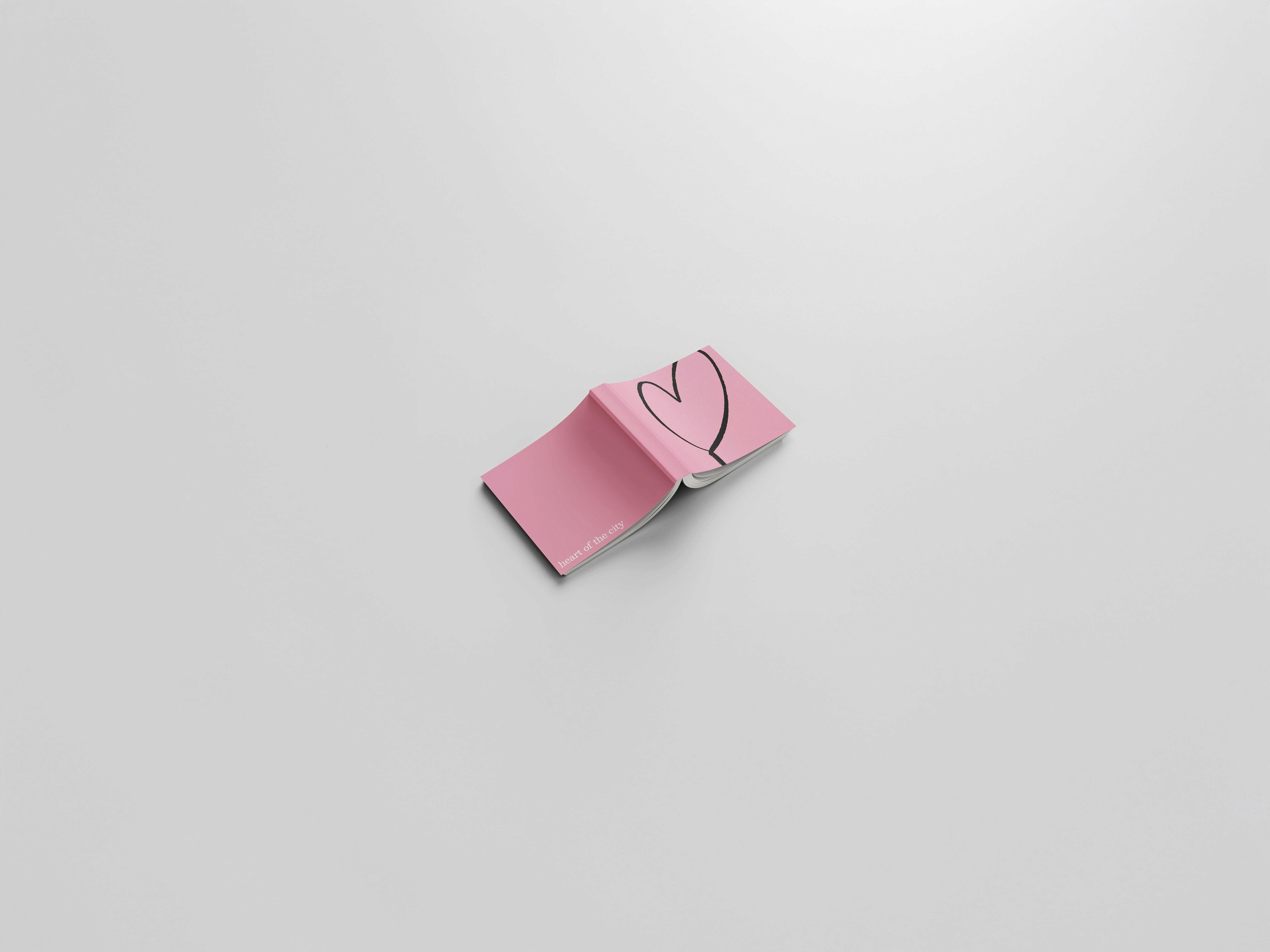 Minimalist pink book titled Heart of the City, opened to a simple black heart illustration. A visual statement on softness, intimacy, and belonging in urban space.