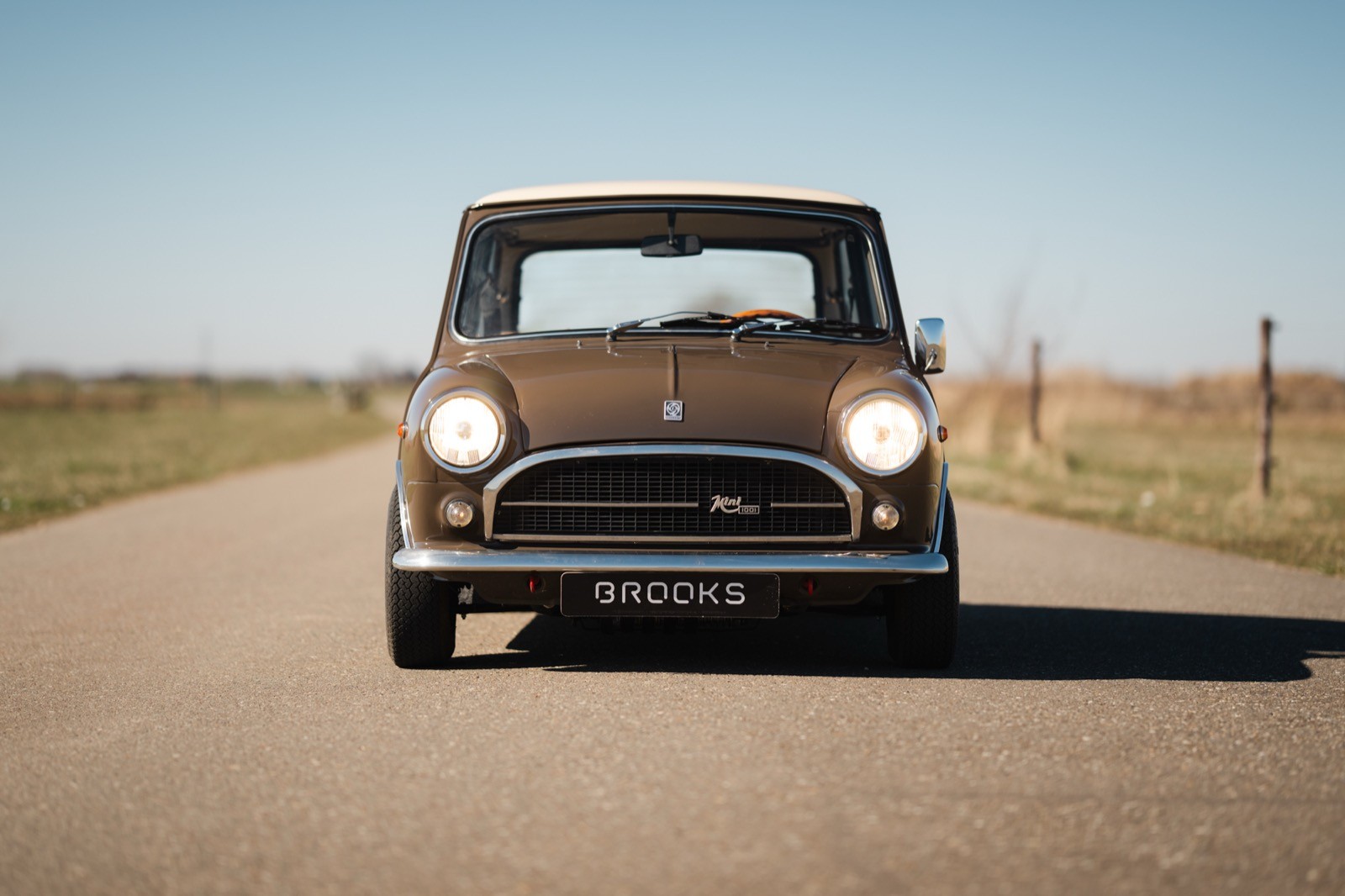 A vintage car on an empty, open road with clear blue skies in the background.