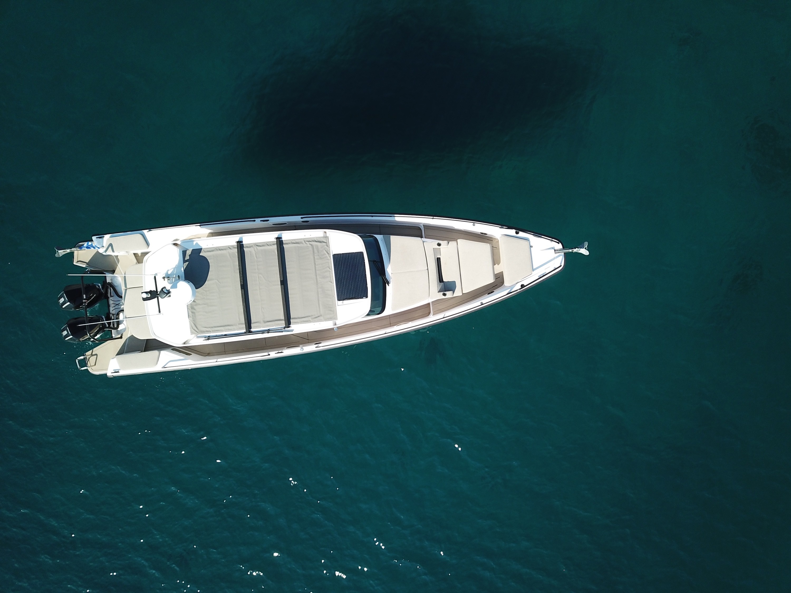 Aerial view of Axopar 37 Zeus motor yacht with white hull and twin outboard engines anchored in crystal-clear turquoise waters.