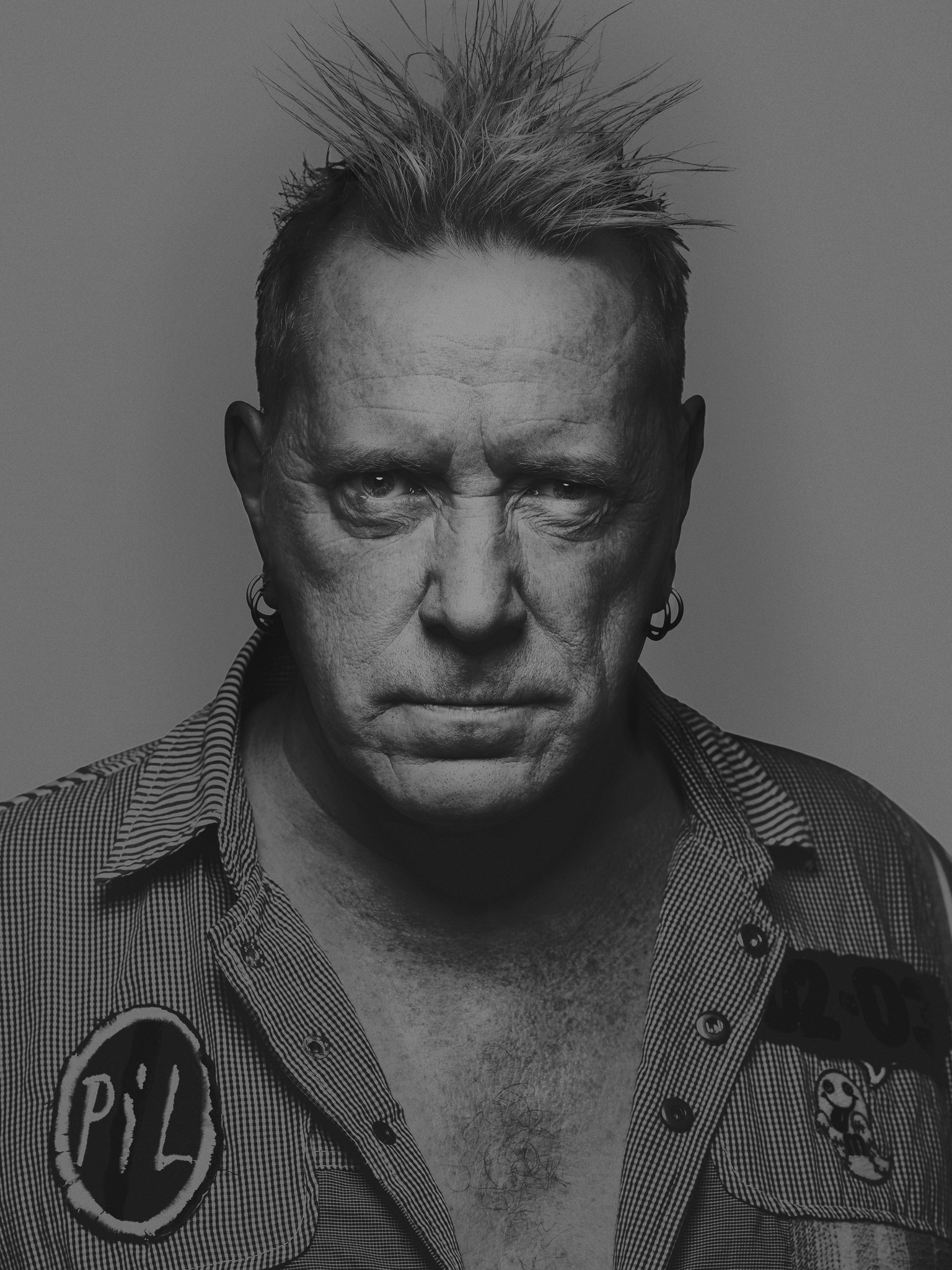 Moody black and white editorial portrait of British musician John Lydon, AKA Johnny Rotten who performed in the Sex Pistols, Public Image Ltd. He has a serious and fixed expression with eye contact to the camera. Shot by photographer Craig Mulcahy in the studio in New Orleans, Louisiana. 