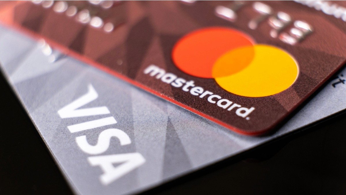 Nahaufnahme übereinanderliegender Kreditkarten: rote Mastercard mit orangen und roten Kreisen und weißer Schrift; graue Visa mit weißer Schrift.