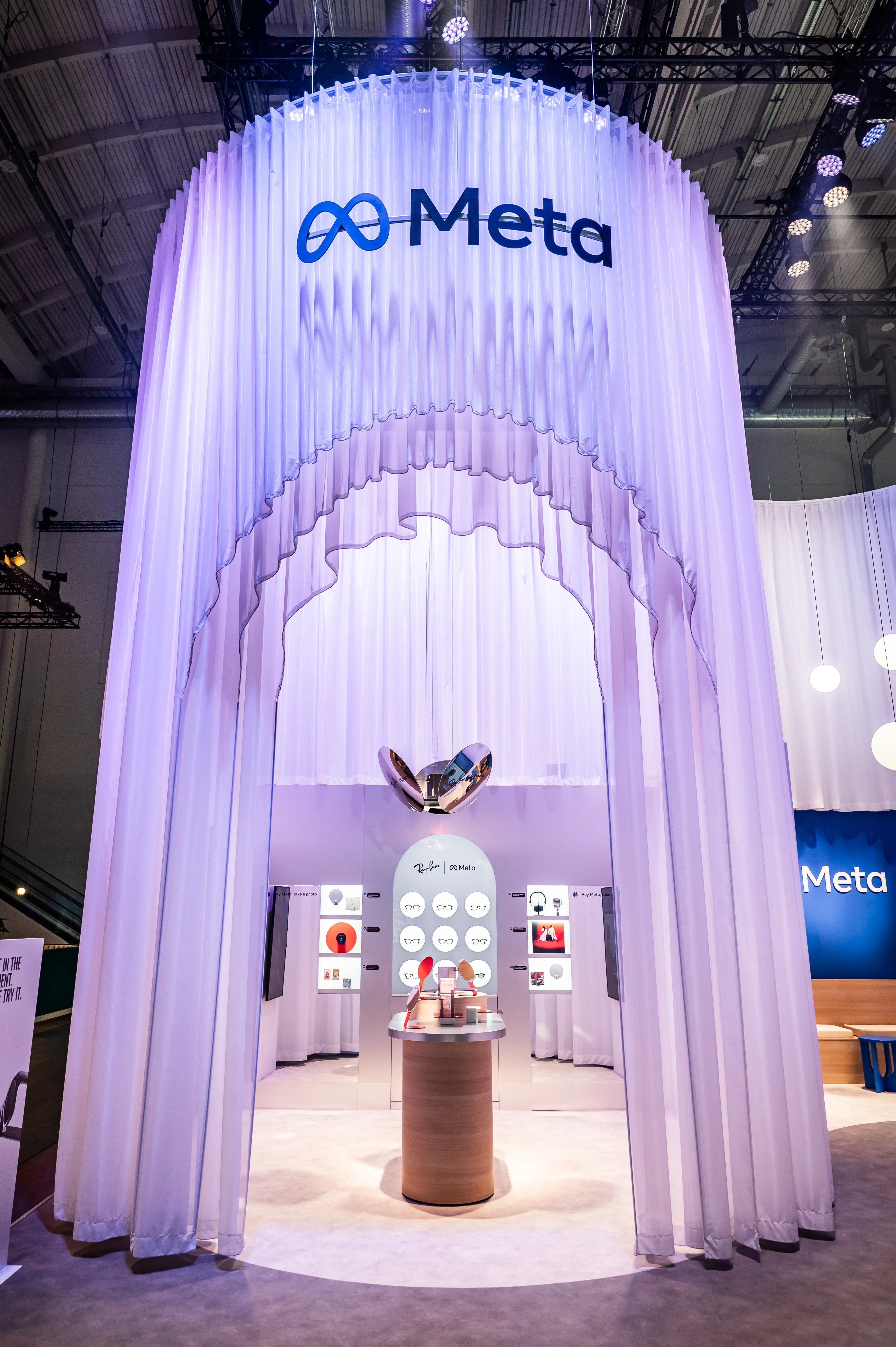 Tall arched entrance of the Meta booth made of white pleated curtains with logo and Ray-Ban display inside.