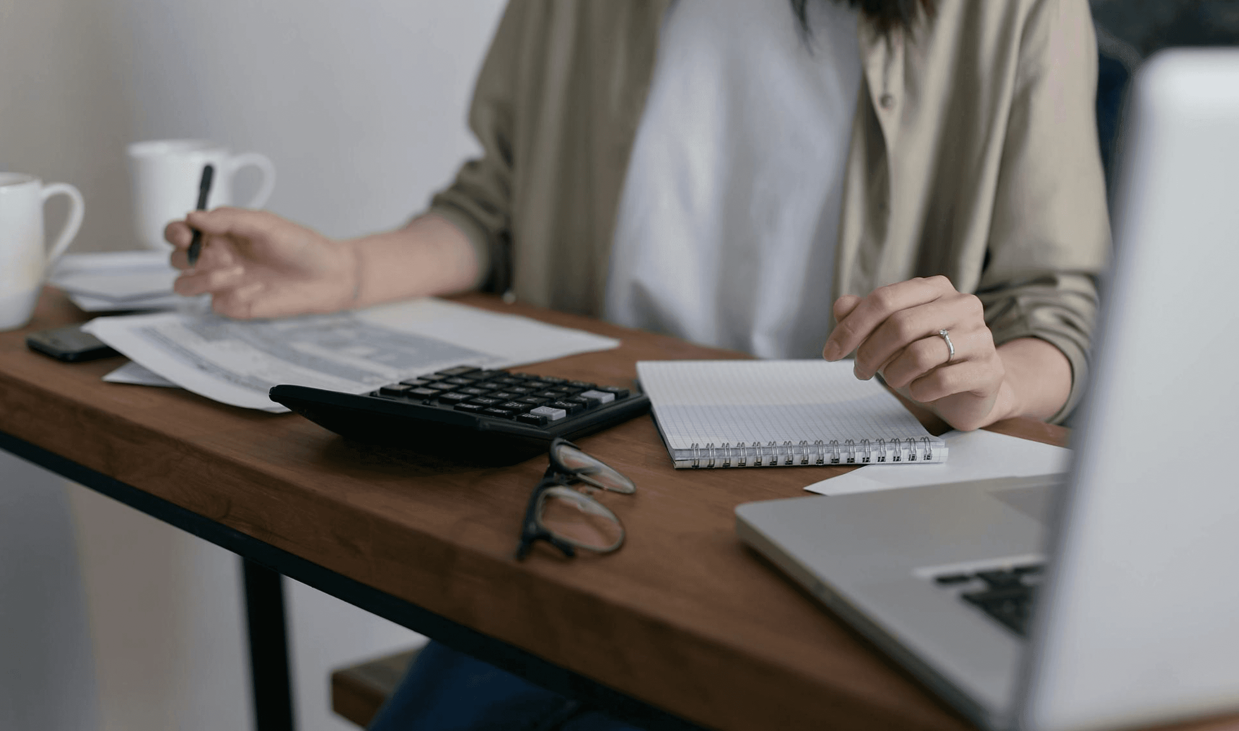 Pessoa em uma mesa com computador, calculadora e papéis