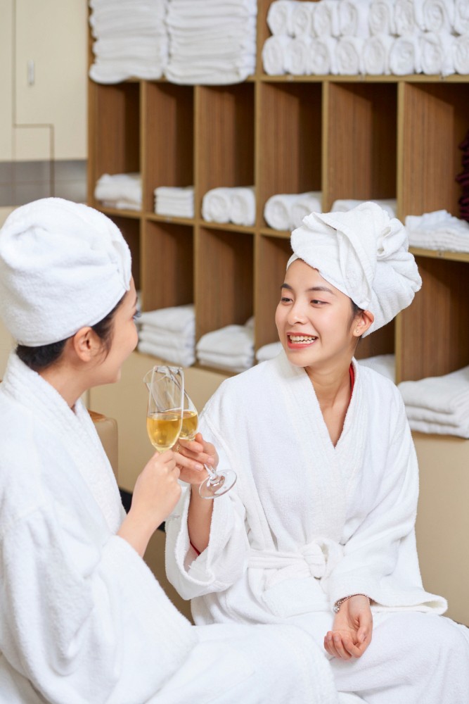 兩位女士在 Attitude Beauty 享受放鬆的美容療程後，穿著浴袍於舒適更衣室內舉杯慶祝。