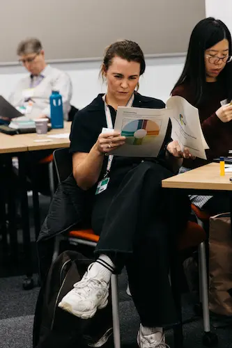 People sitting at a table, writing in notebook.