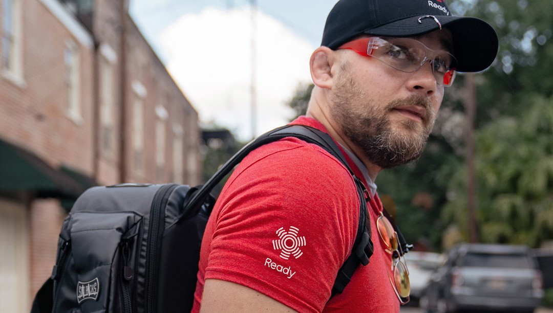 Ready Responder in a red branded shirt and black cap carrying a medical backpack outdoors.