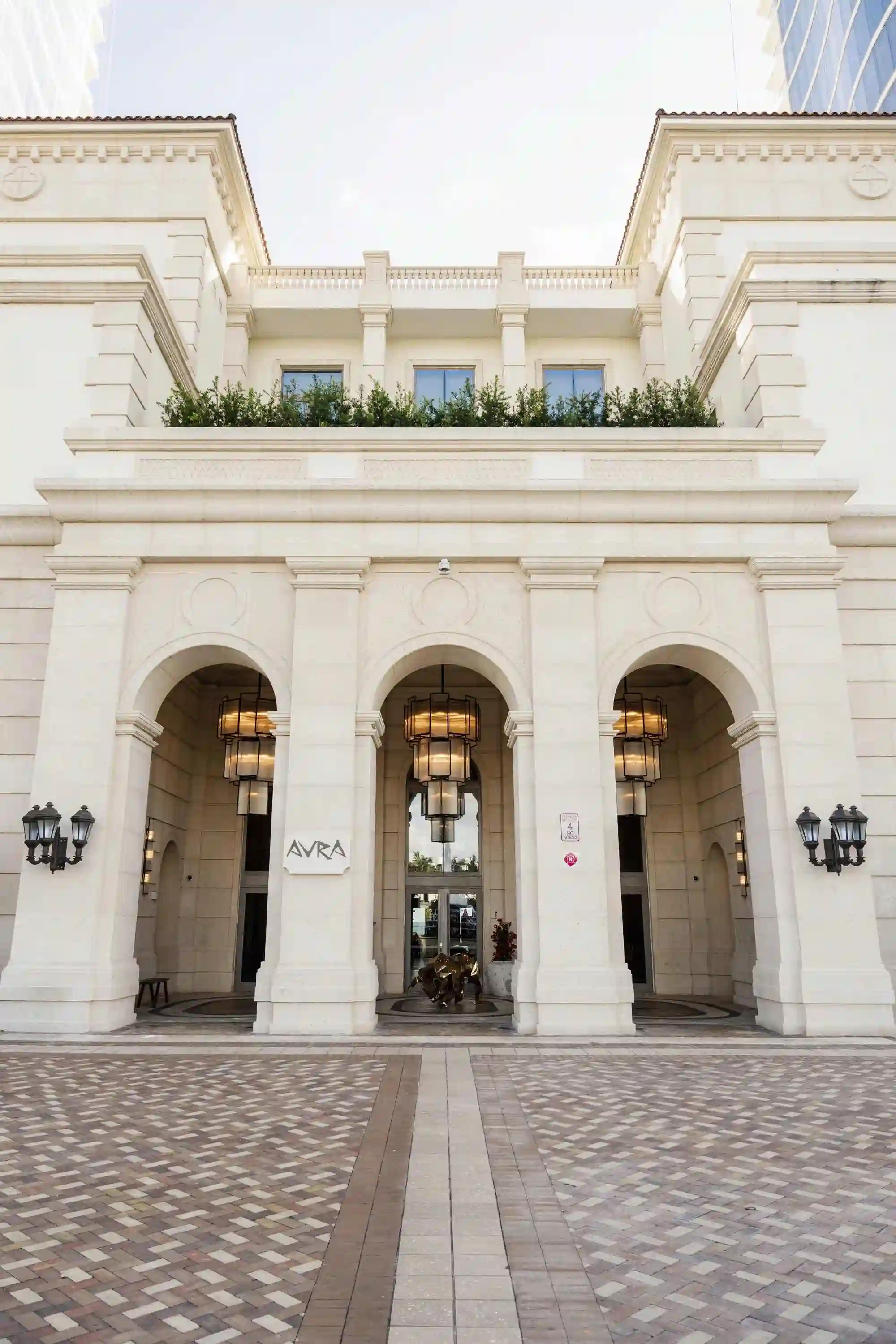 Entrance of a grand building with archways, flanked by plaques and a tiled pathway leading up to the doors.