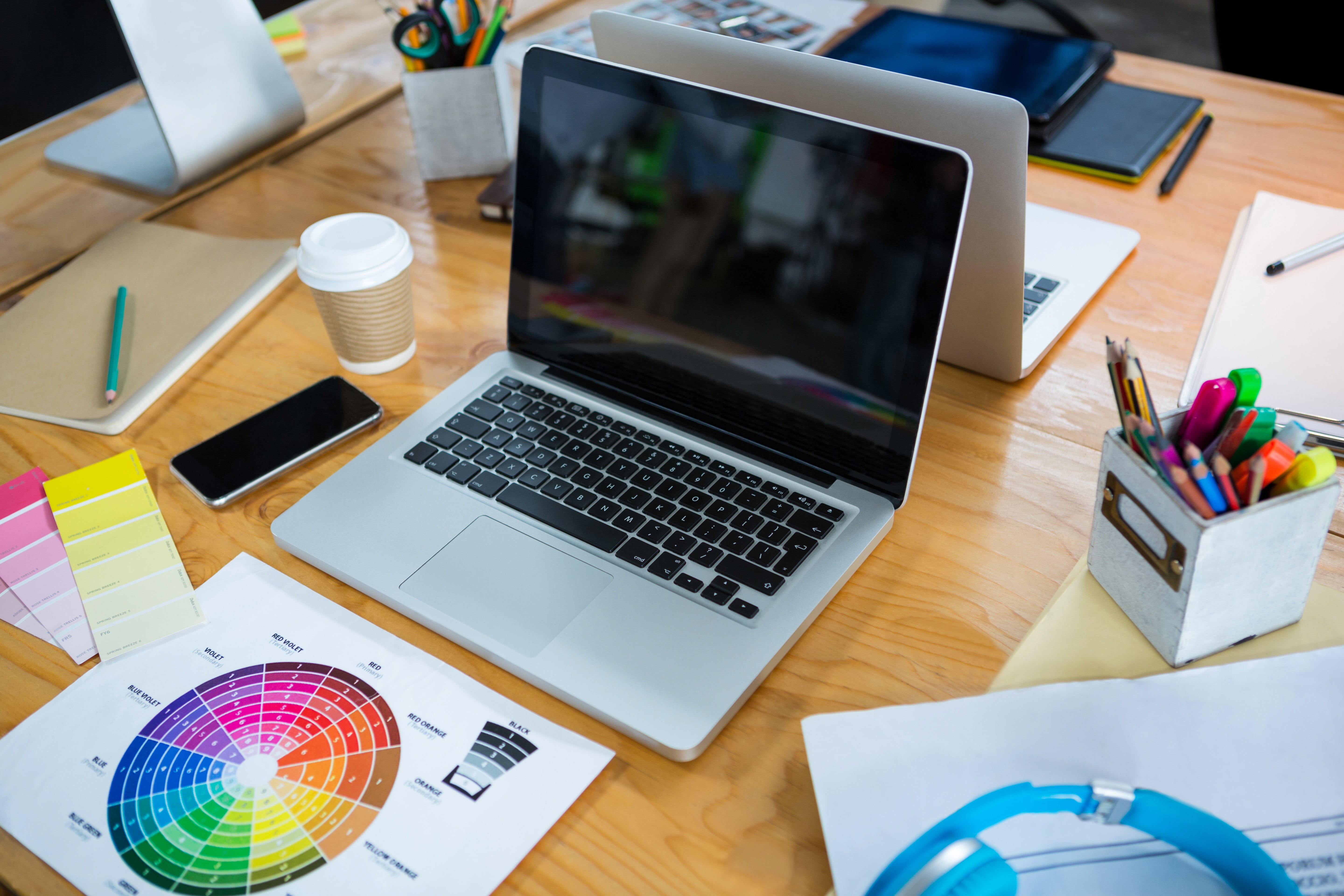 Graphic design workspace with laptop, color wheel, and art supplies