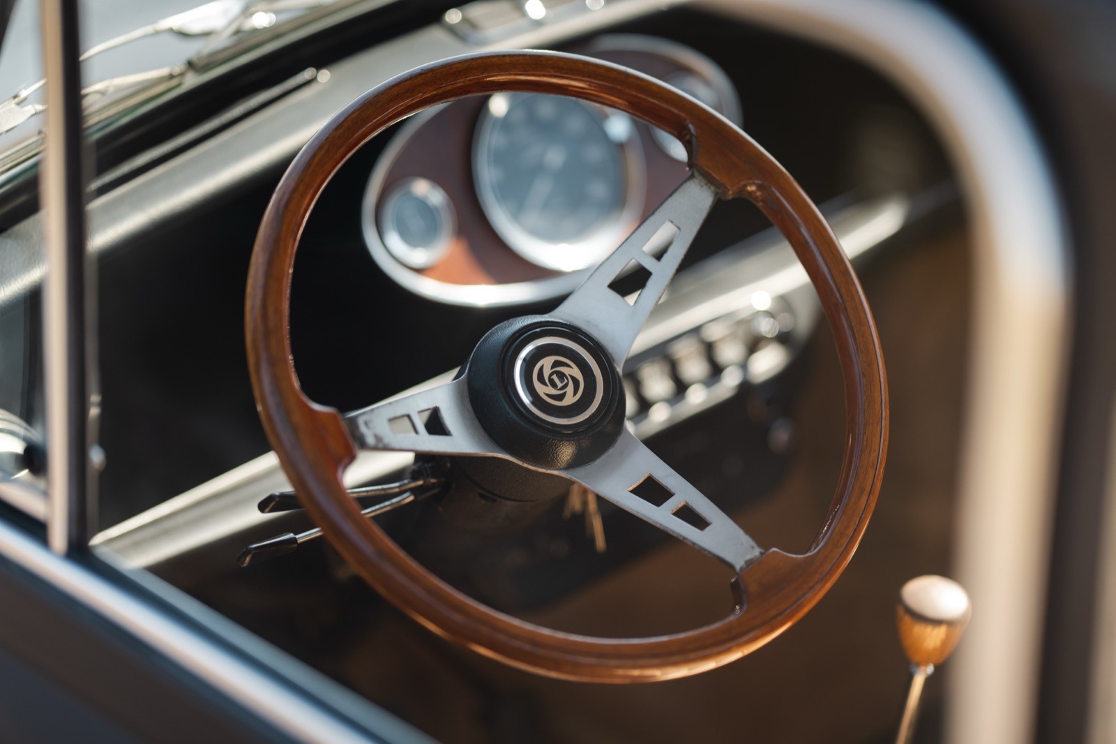 Close-up of a classic car's interior showing a wooden steering wheel and dashboard with gauges.