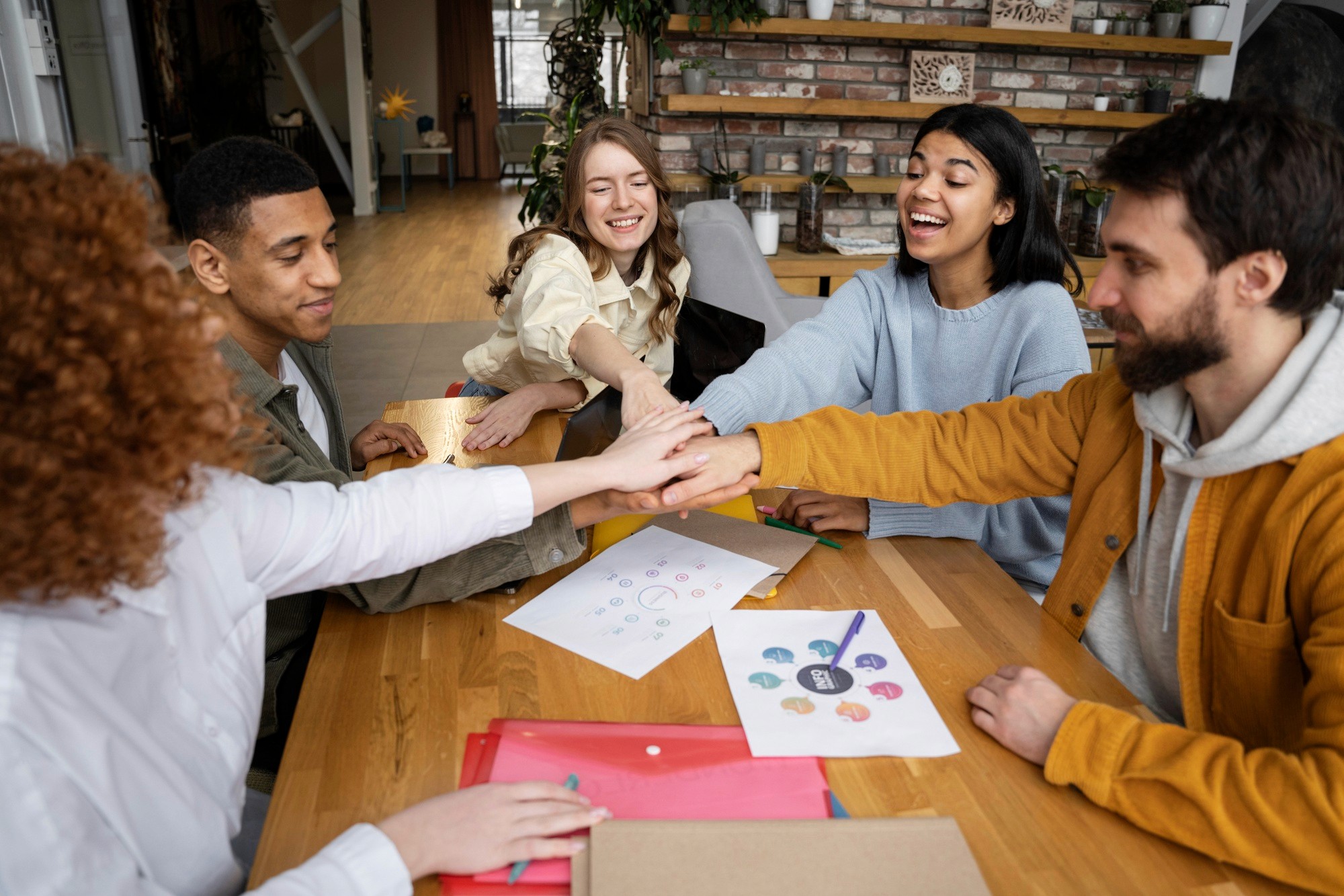 Diverse team stacking hands over a table, celebrating collaboration and shared goals.