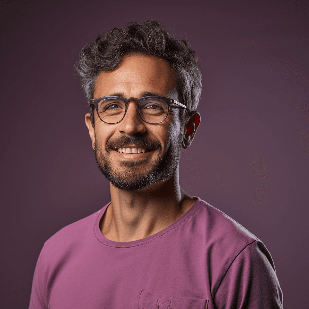 “Portrait of a smiling man with short wavy hair and glasses, wearing a pink T-shirt against a soft purple studio background.