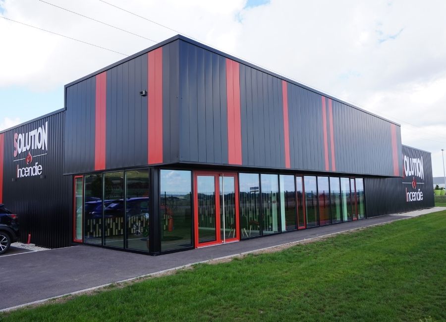 Façade moderne d’un bâtiment industriel avec bardage métallique noir et rouge.