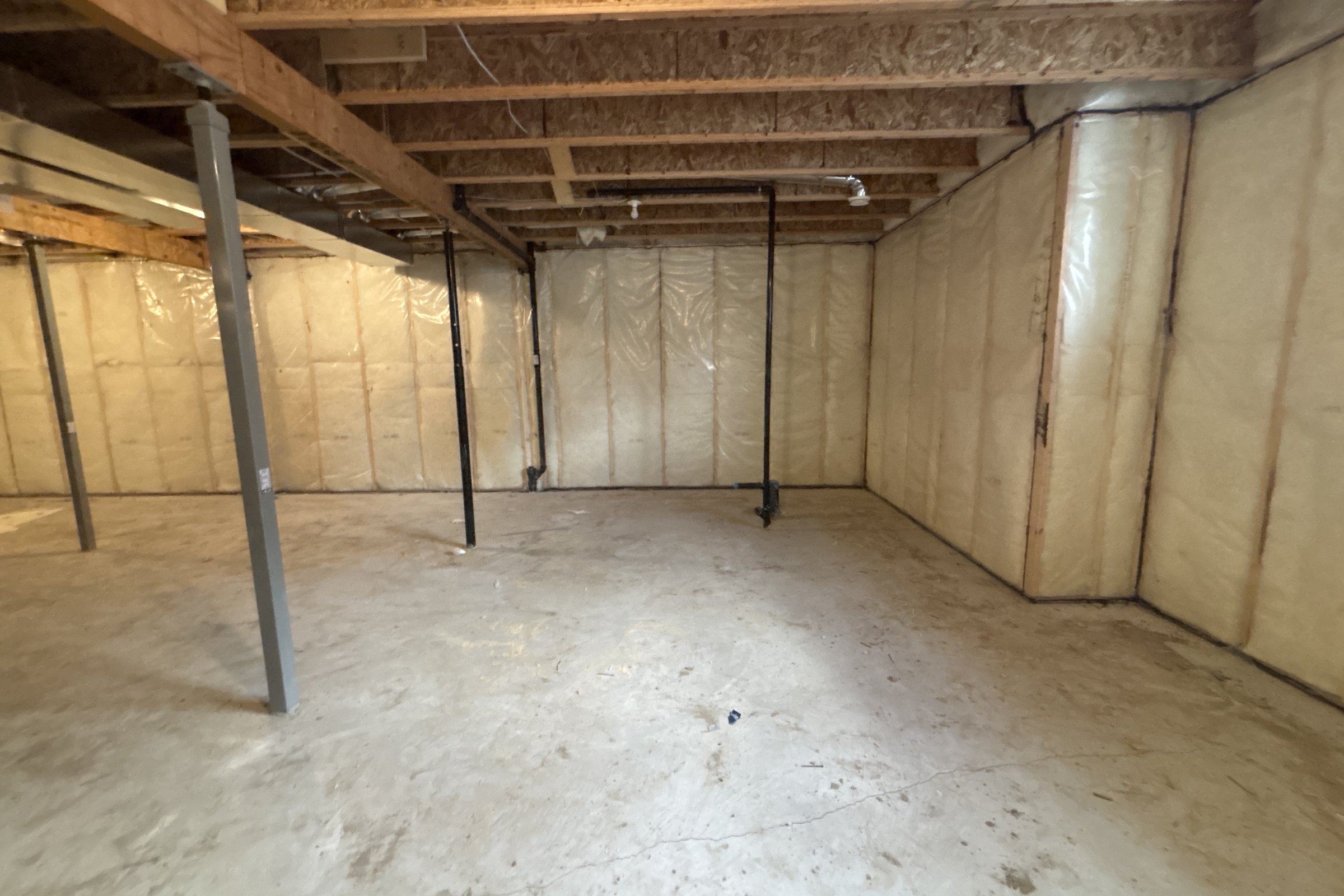 Unfinished basement before: open joists and support posts where the kitchen now stands
