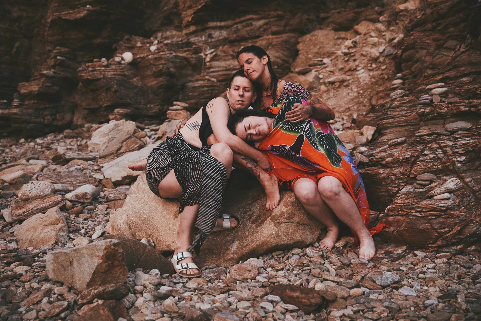 three women huddled on rocky shore — lifestyle photography by Tom Kubik
