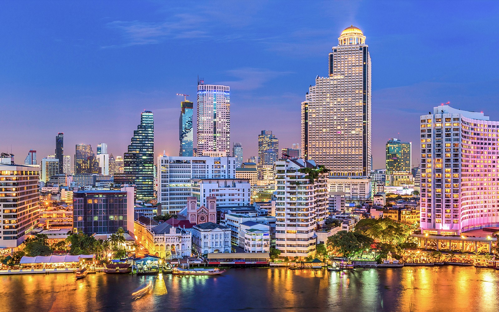 Bangkok skyline with Chao Phraya River in the foreground at dusk.
