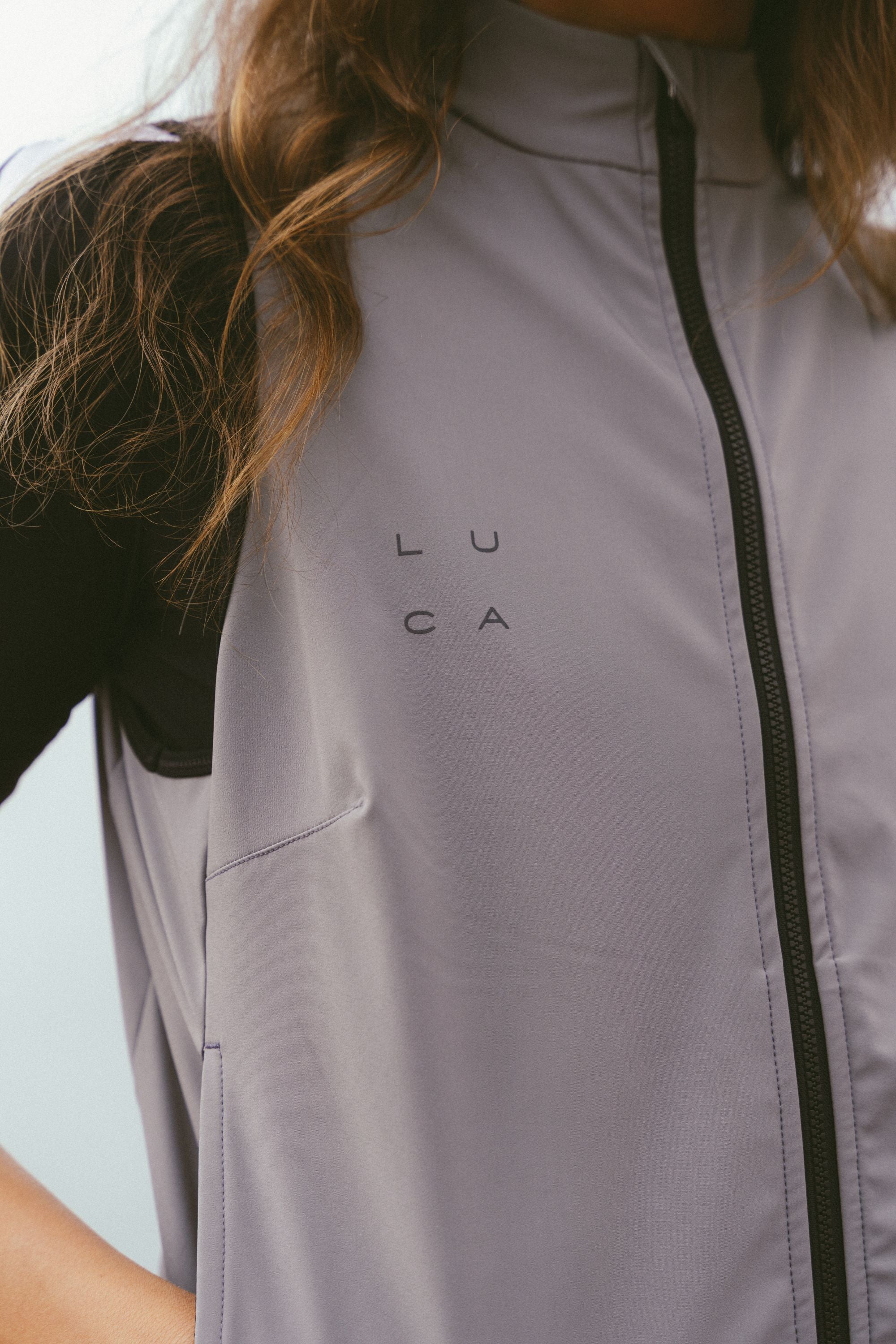 Close-up-detail-of-the-taupe-grey-cycling-gilet-highlighting-the-minimal-square-arraged-LUCA-logo-on-chest-The-image-also-shows-the-technical-fabric-and-the-subtle-side-pocket-stitching