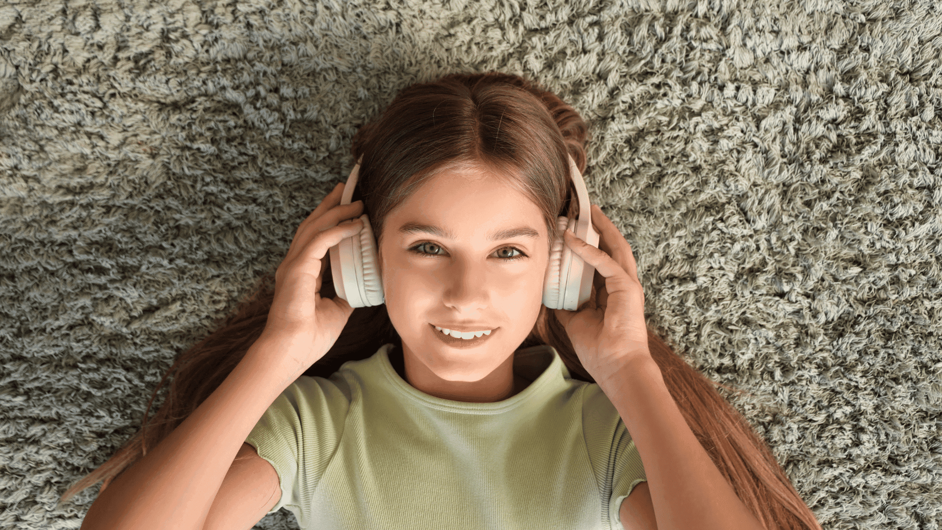 A girl lying on a soft surface, wearing headphones and smiling at the camera while listening to HushAway®’s Sound Sanctuary.