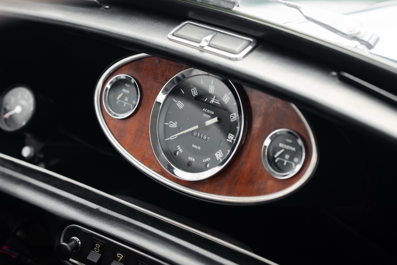Close-up of a vintage car dashboard, featuring a classic speedometer with wood accents and stylish dials.